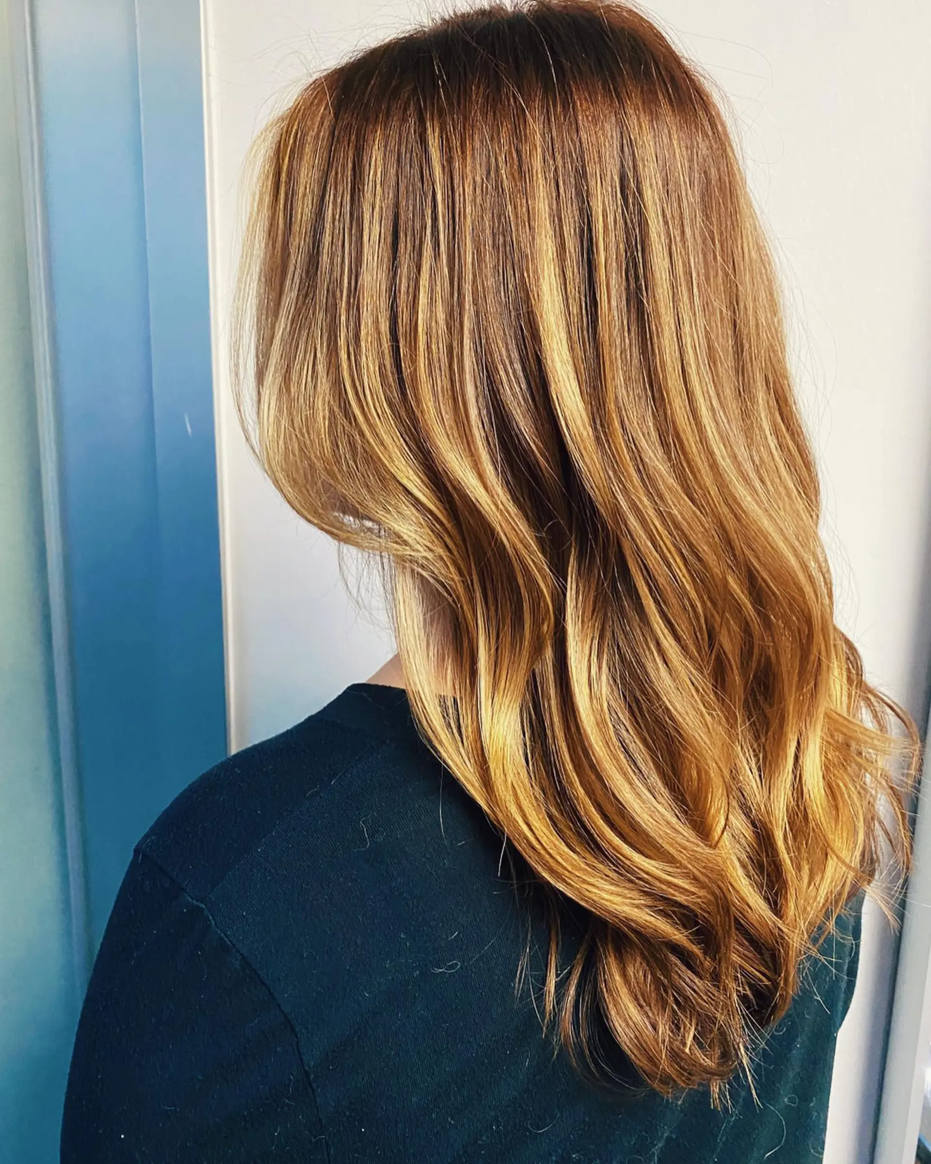 Long warm auburn hair styled with dimensional golden highlights and soft waves through the lengths. 1