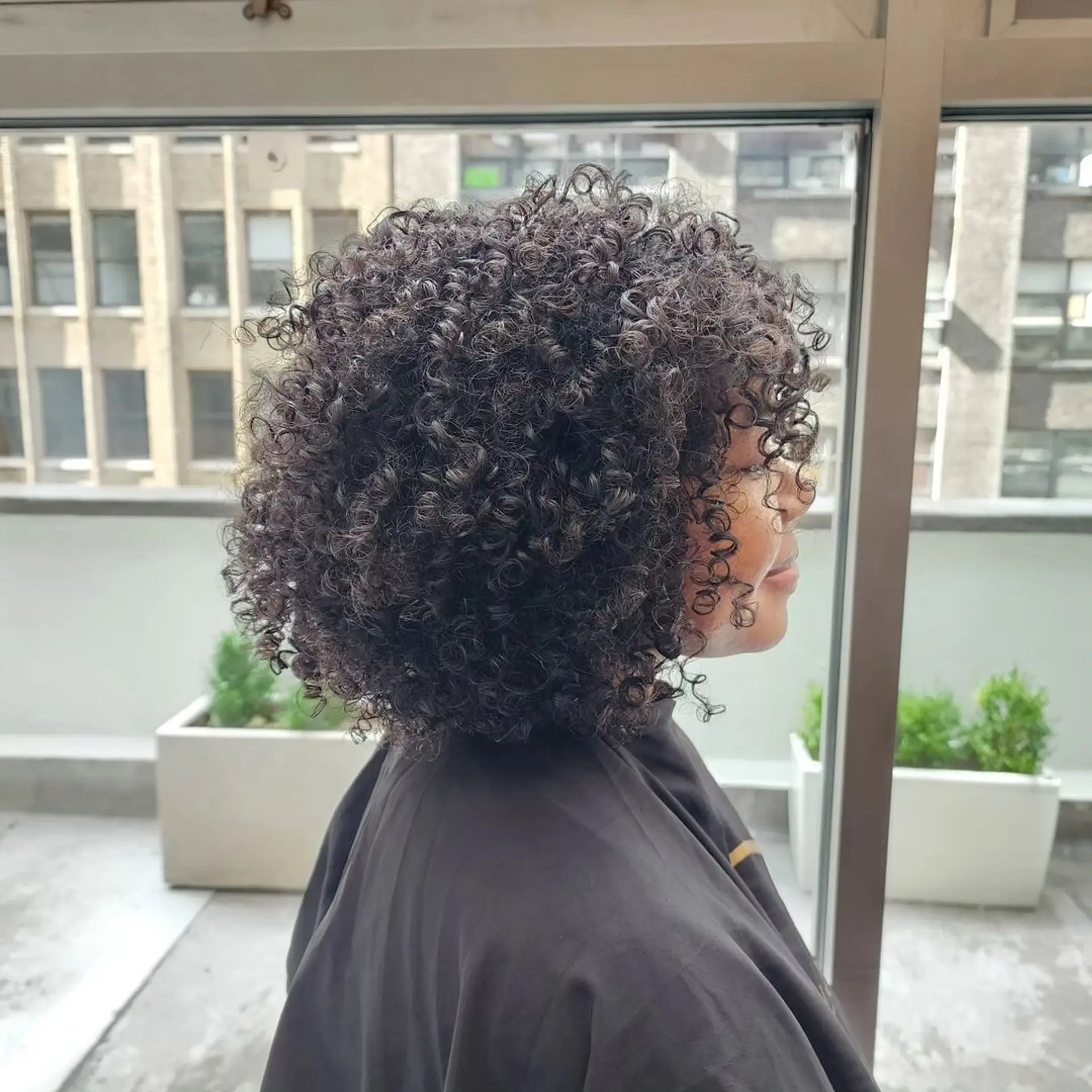 Medium length, naturally curly hair with tight, defined curls and a voluminous appearance. The curls fall around the face, complemented by natural fringe bangs. 2