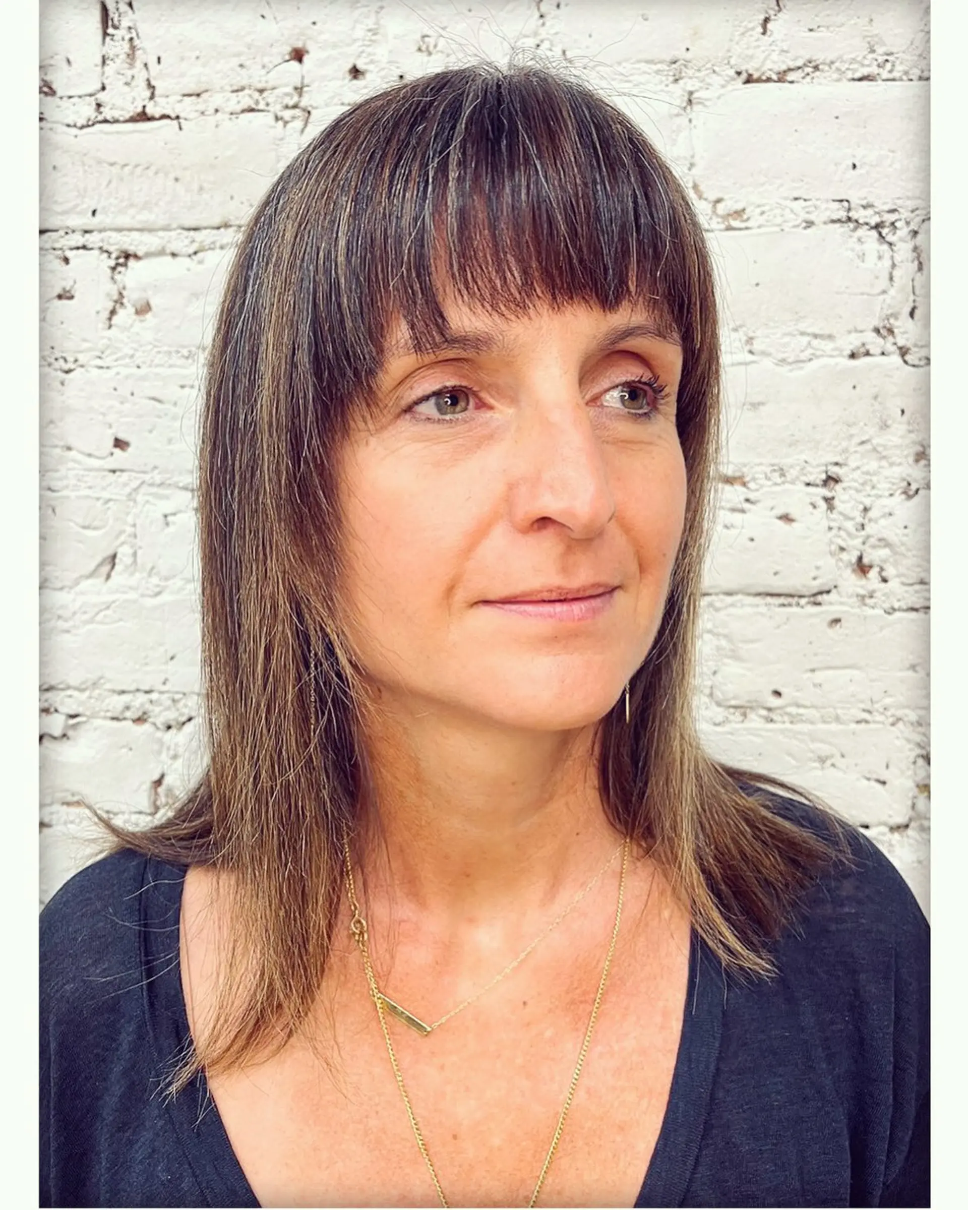 A shoulder-length haircut in cool ash brown tones, styled with straight-across textured bangs and soft ends. 1