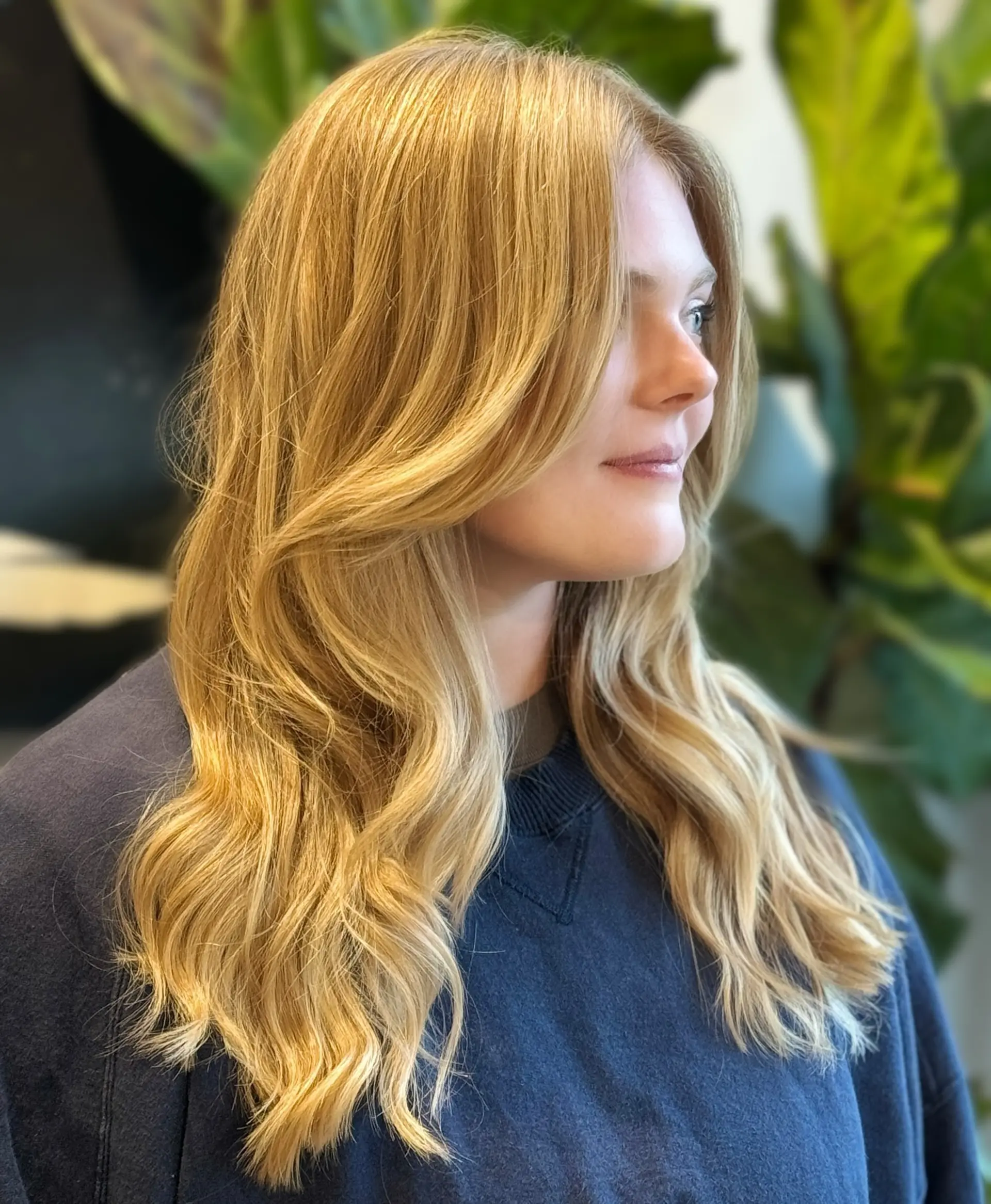 Long sun-kissed golden blonde hair styled in soft, bouncy waves with face-framing curtain layers. 1