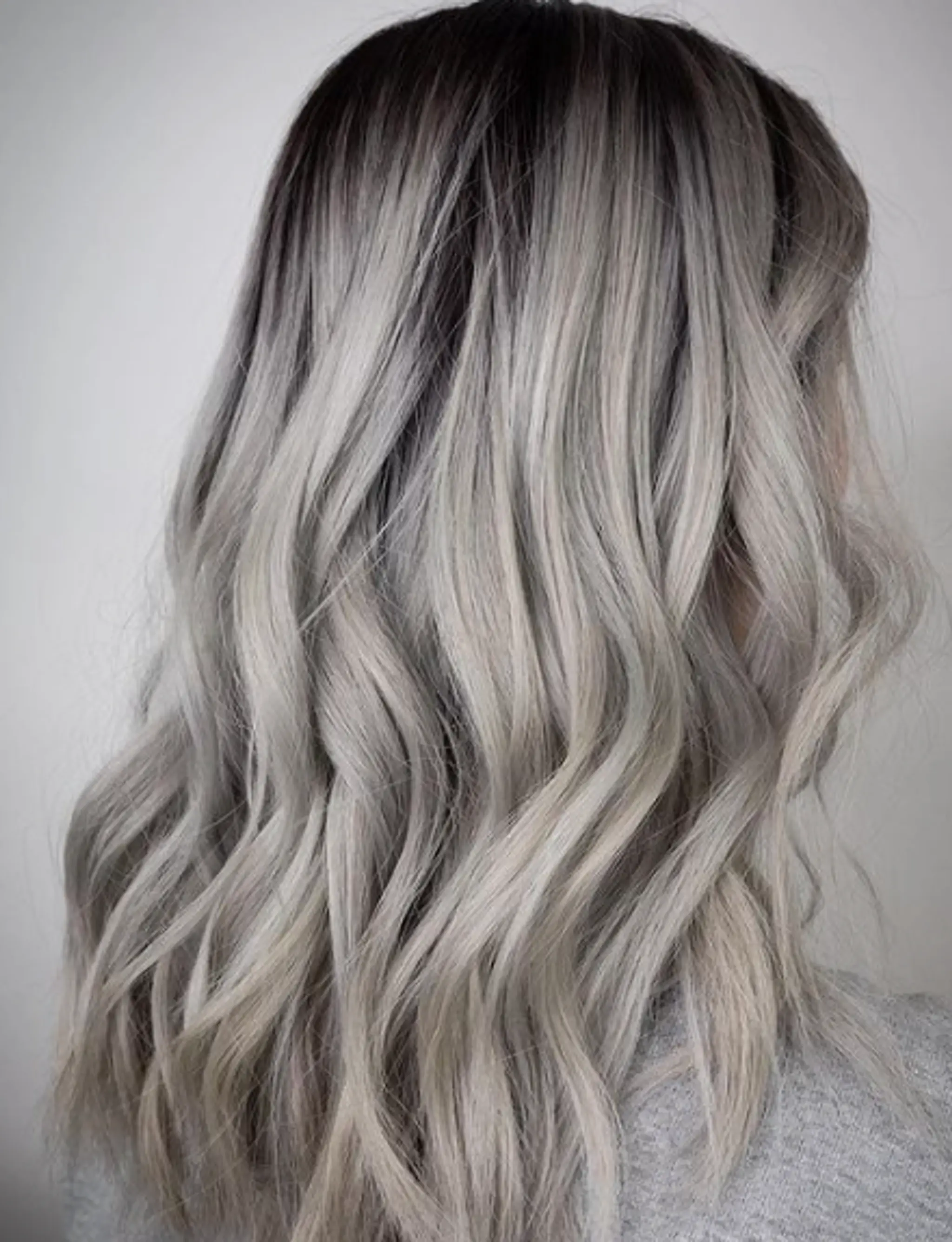 Medium-length, wavy hair with dark roots fading into icy platinum silver in an elegant ombre.