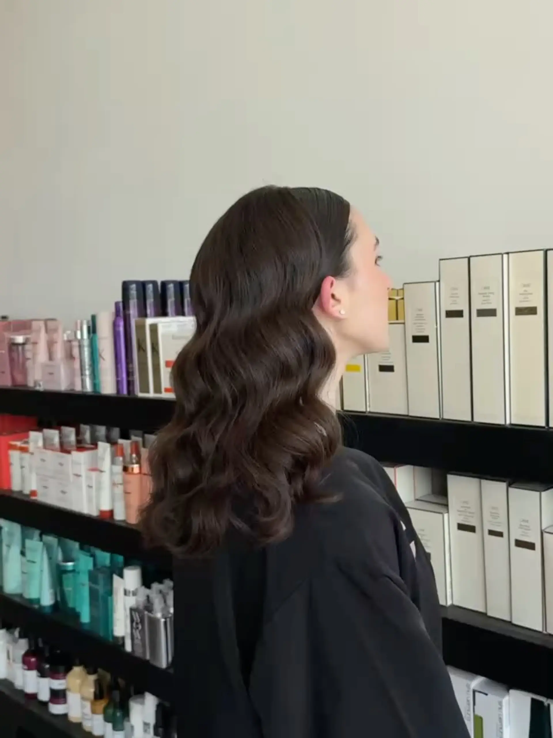Medium-length dark brunette hair styled into sculpted, glossy Hollywood glam waves tucked neatly behind the ear. 1