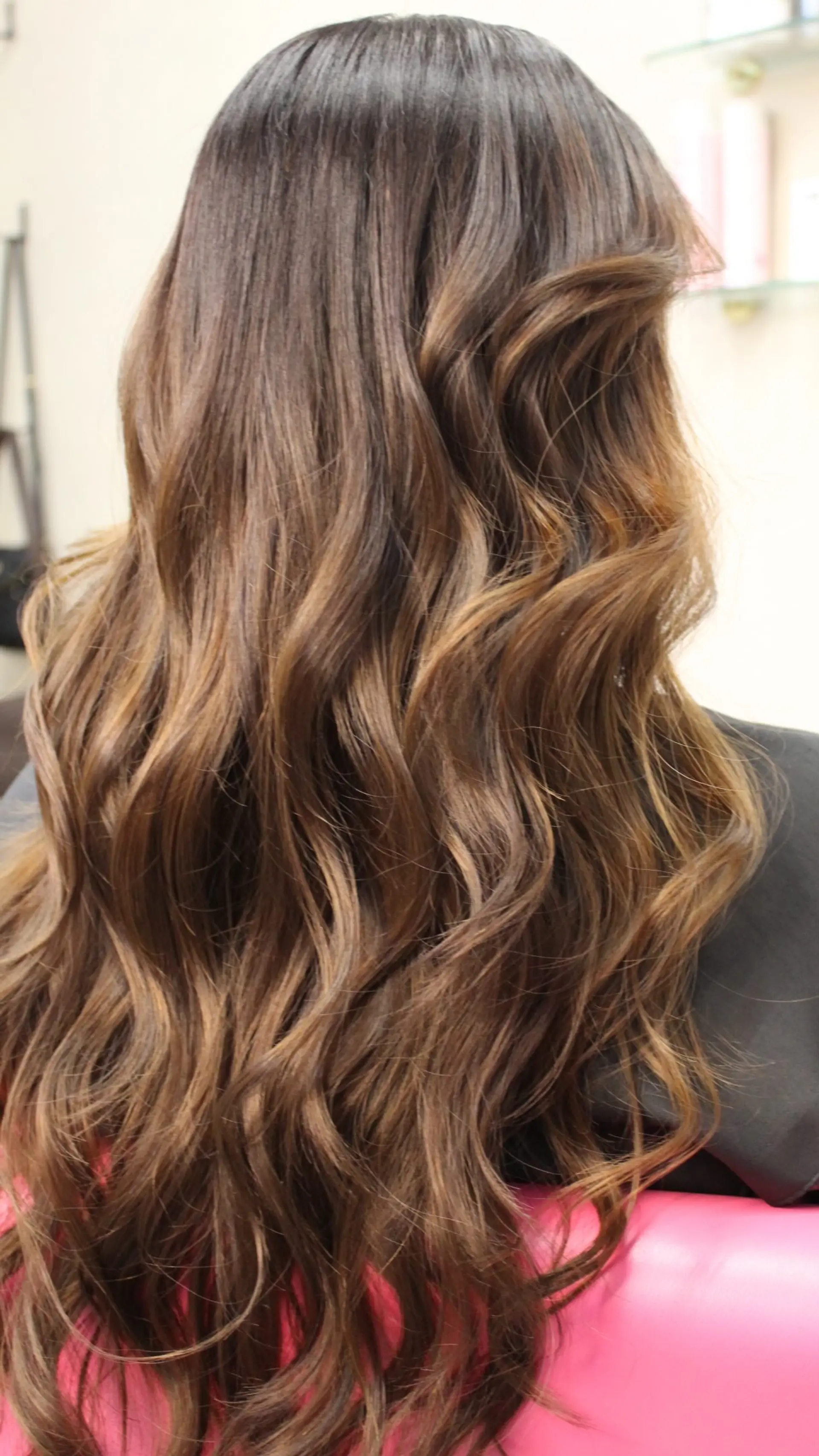 Long dimensional brunette hair styled in loose, textured salon waves with subtle warm caramel balayage accents. 1