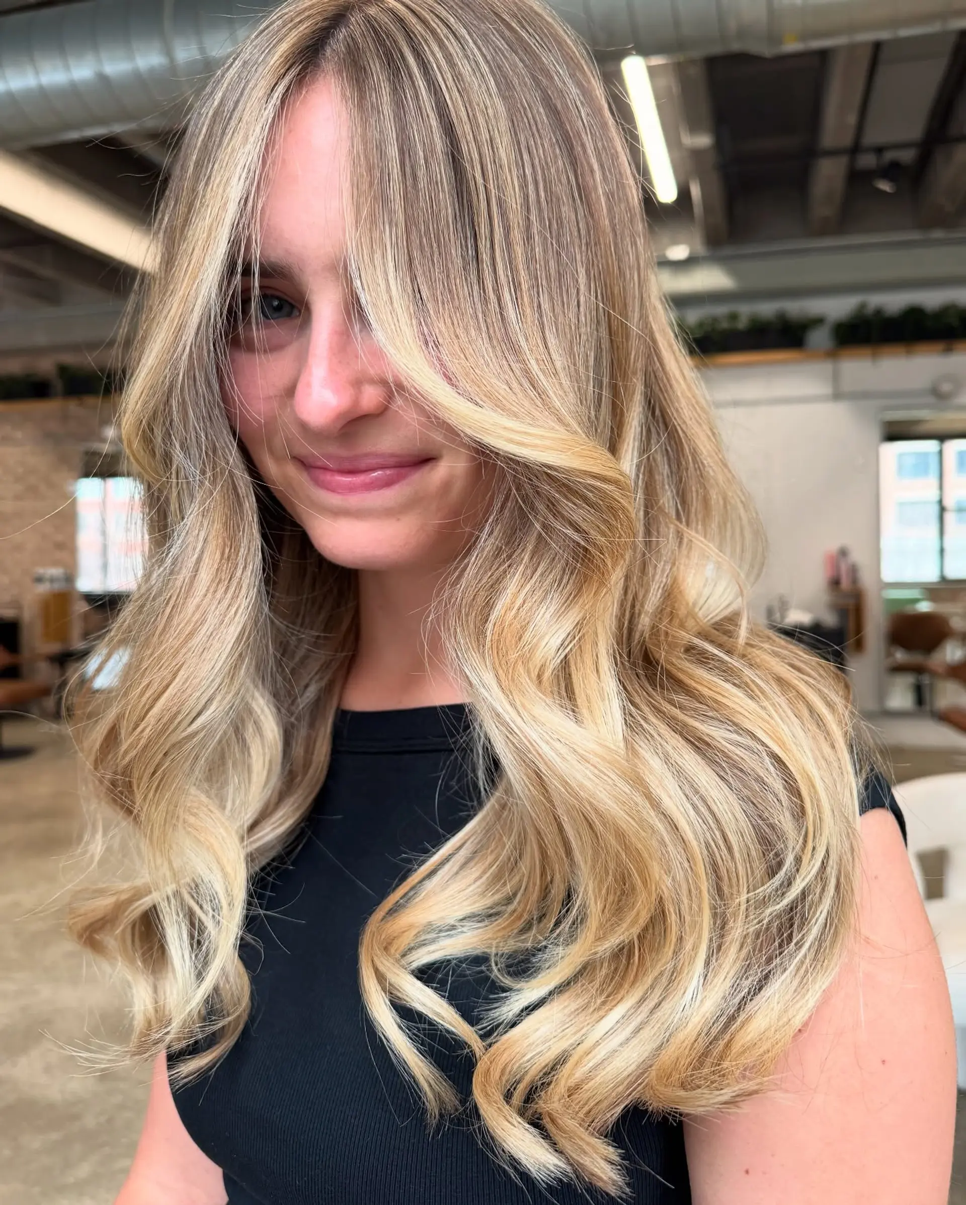 A long, wavy hairstyle with gorgeous blonde balayage, long layers, and face-framing curtain bangs for a voluminous and soft look. 2