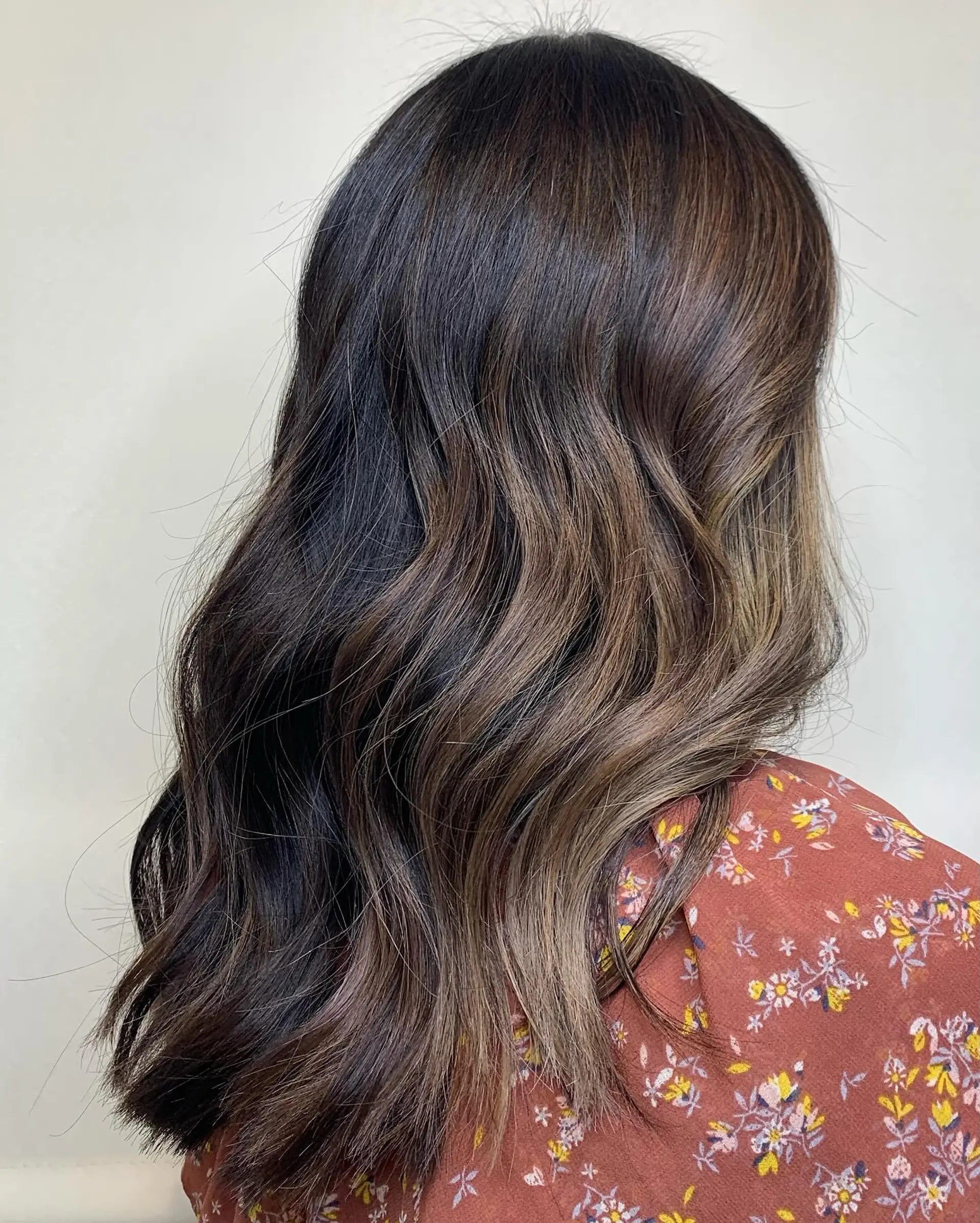 Long dark brown hair enhanced with soft milk chocolate balayage highlights and styled into loose waves. 1