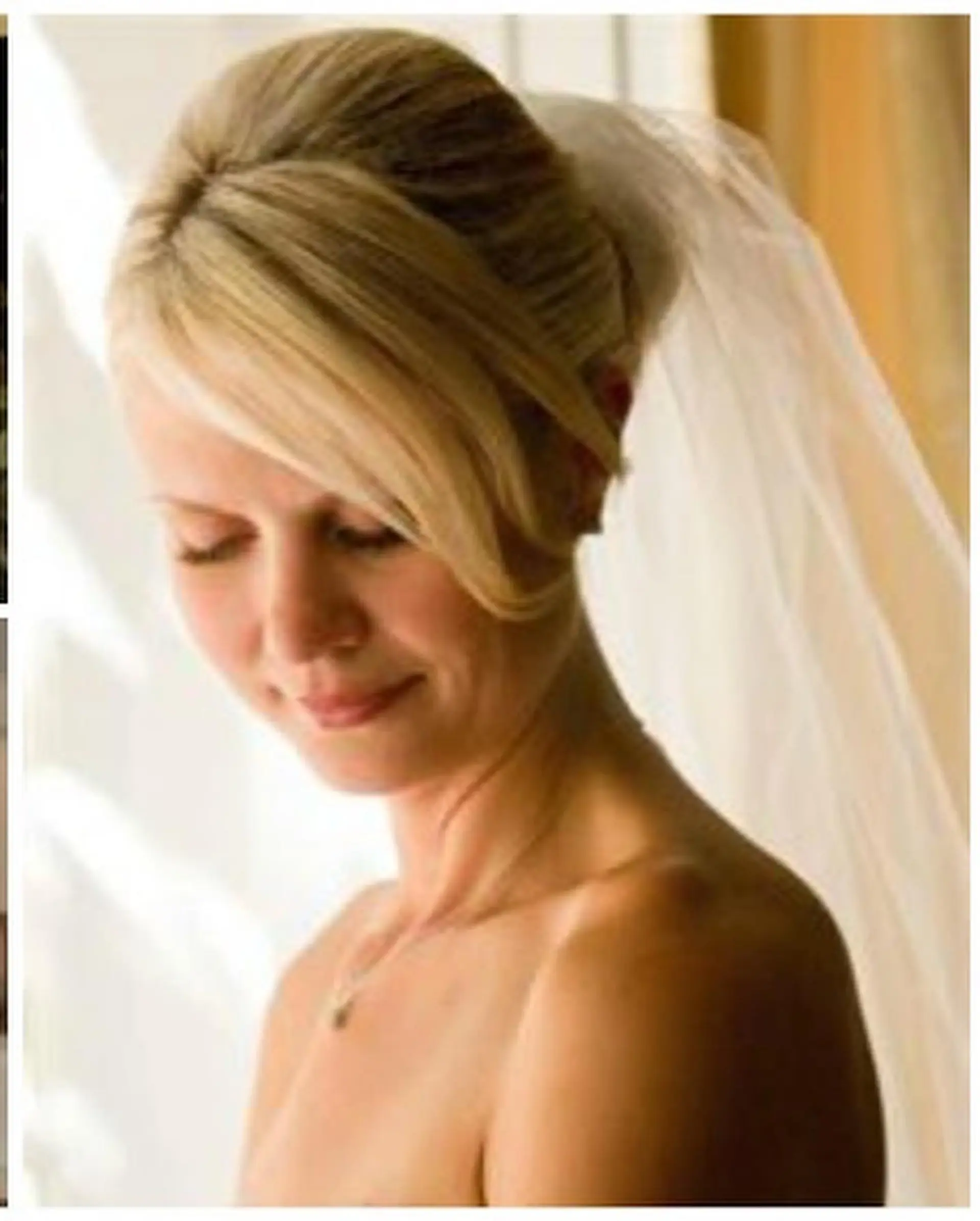 A classic bridal updo featuring gentle crown volume, sleek side-swept bangs, and an attached wedding veil. 1