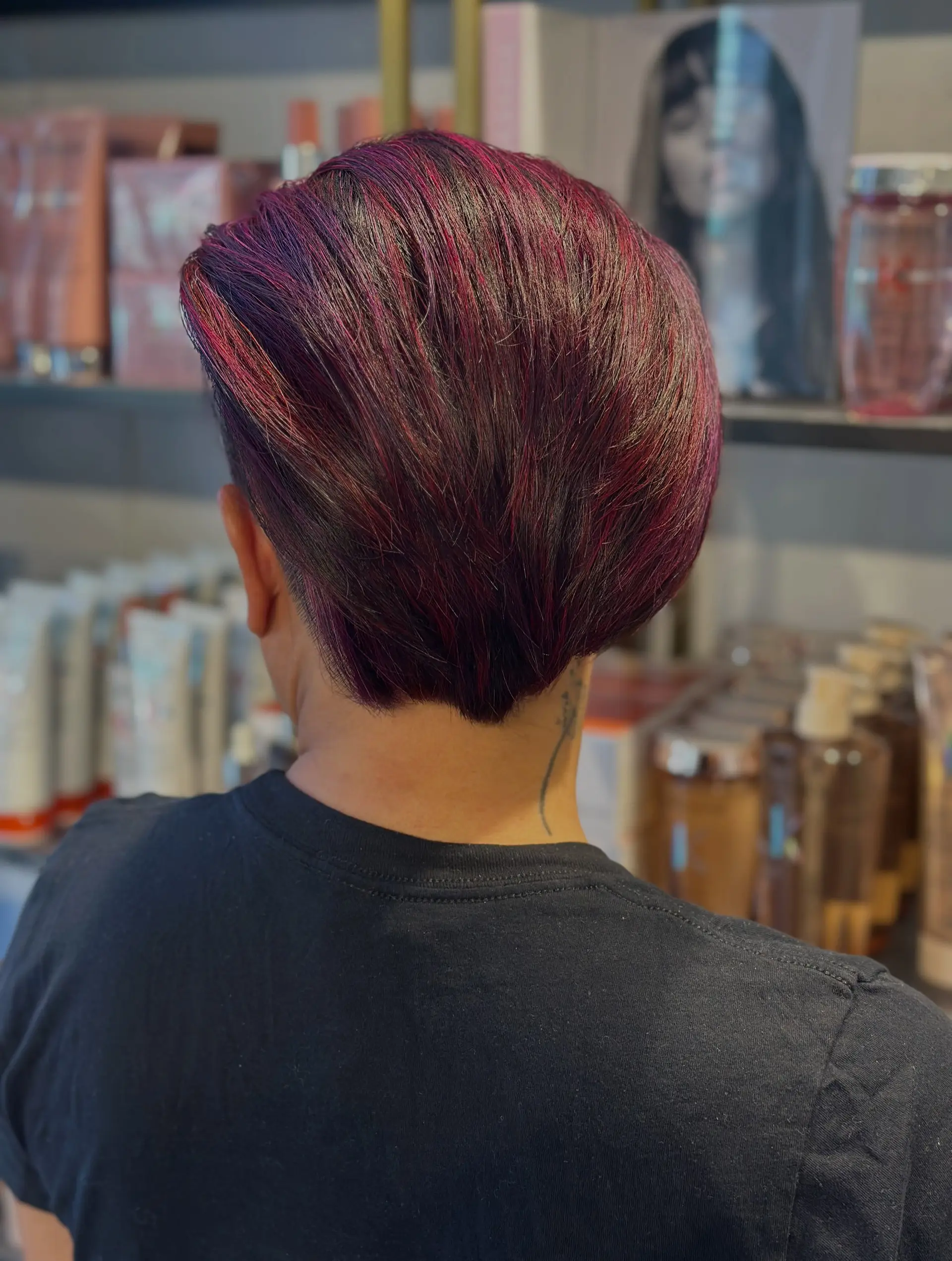 A short, tapered pixie cut styled swept back with vibrant multi-tonal magenta, purple, and red hues. 1