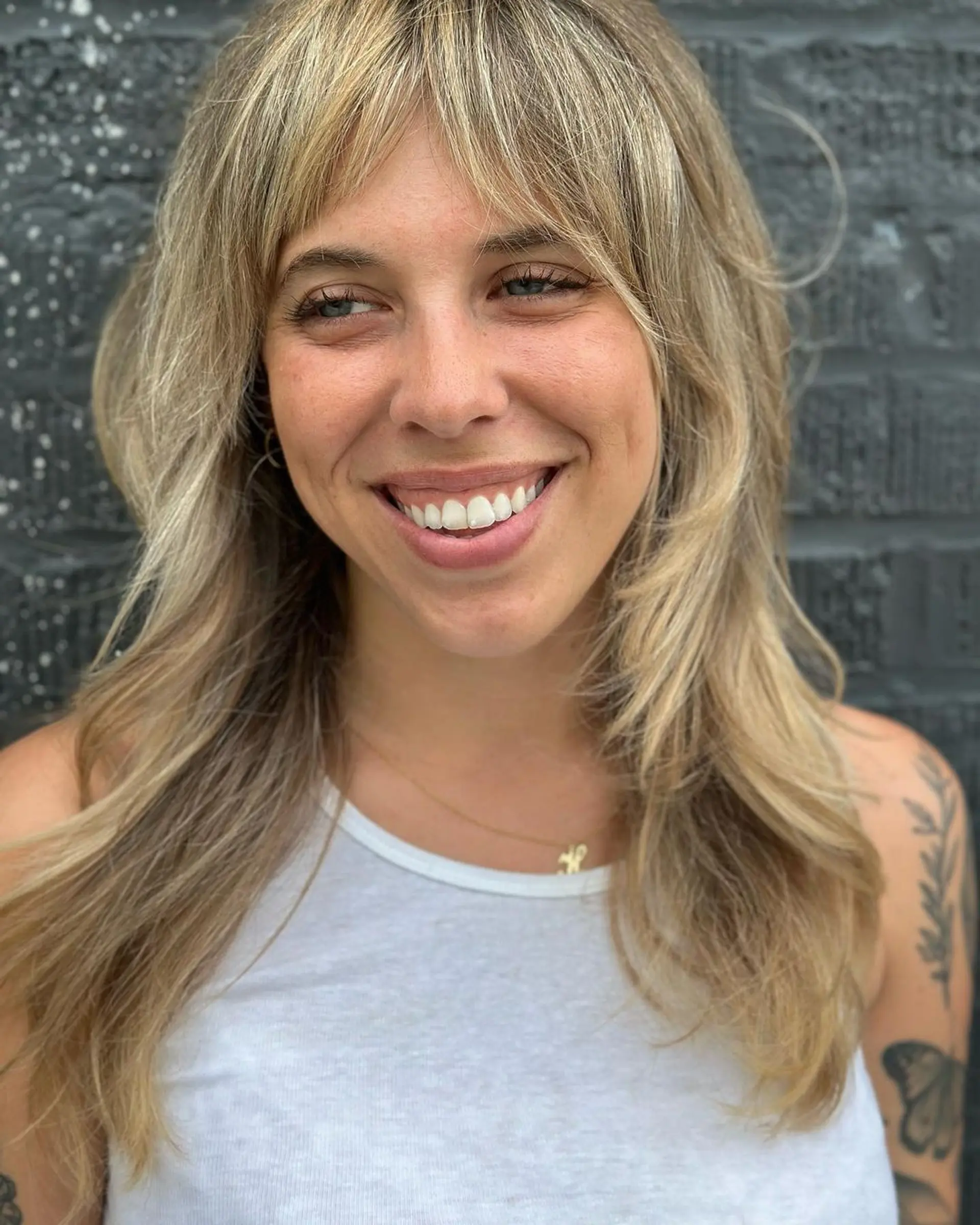 Long wavy blonde hair with multi-tonal highlights, curtain bangs, and a layered cut. 3