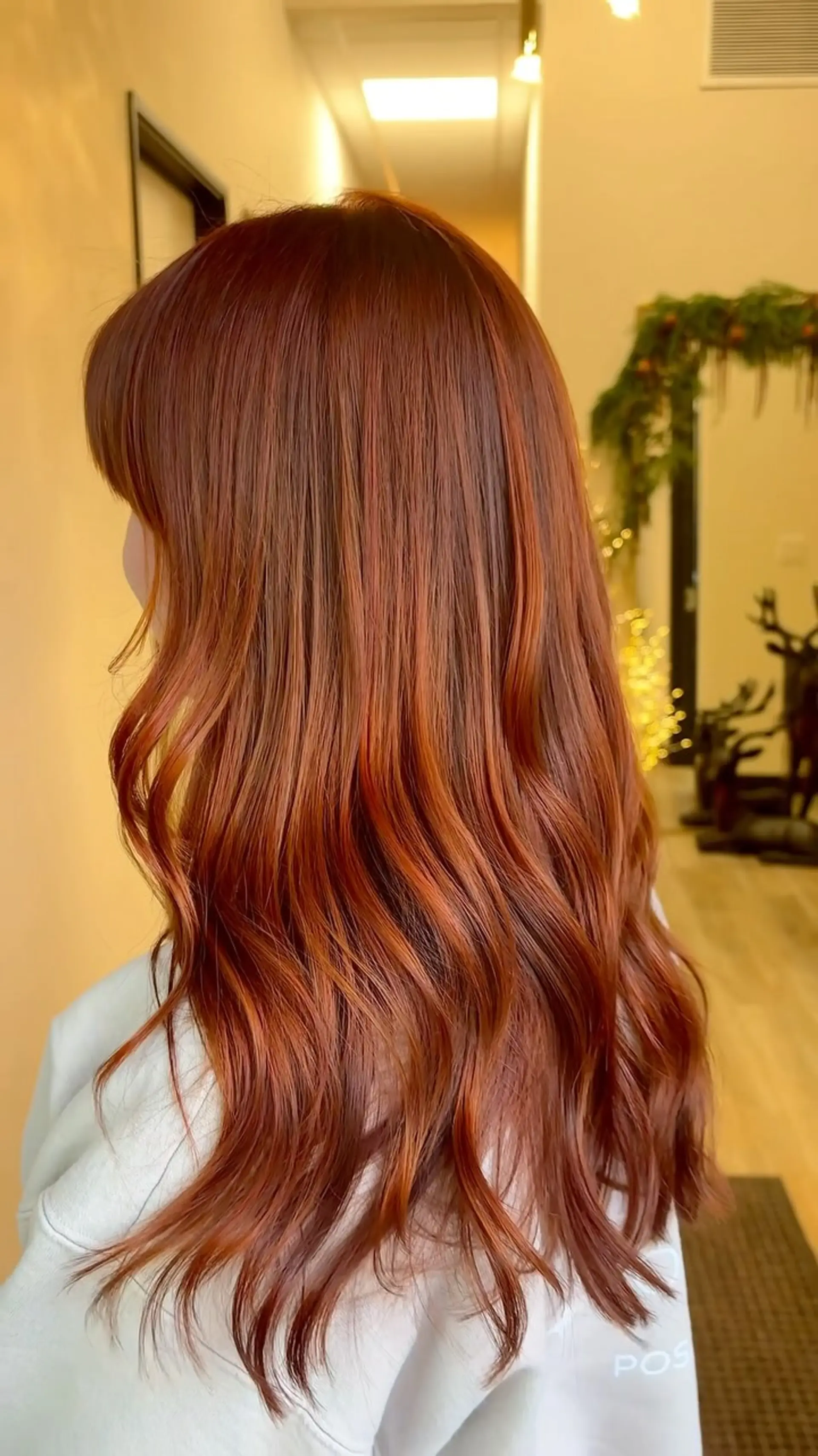 Long, glossy copper hair styled into loose waves with soft fringe bangs. 1