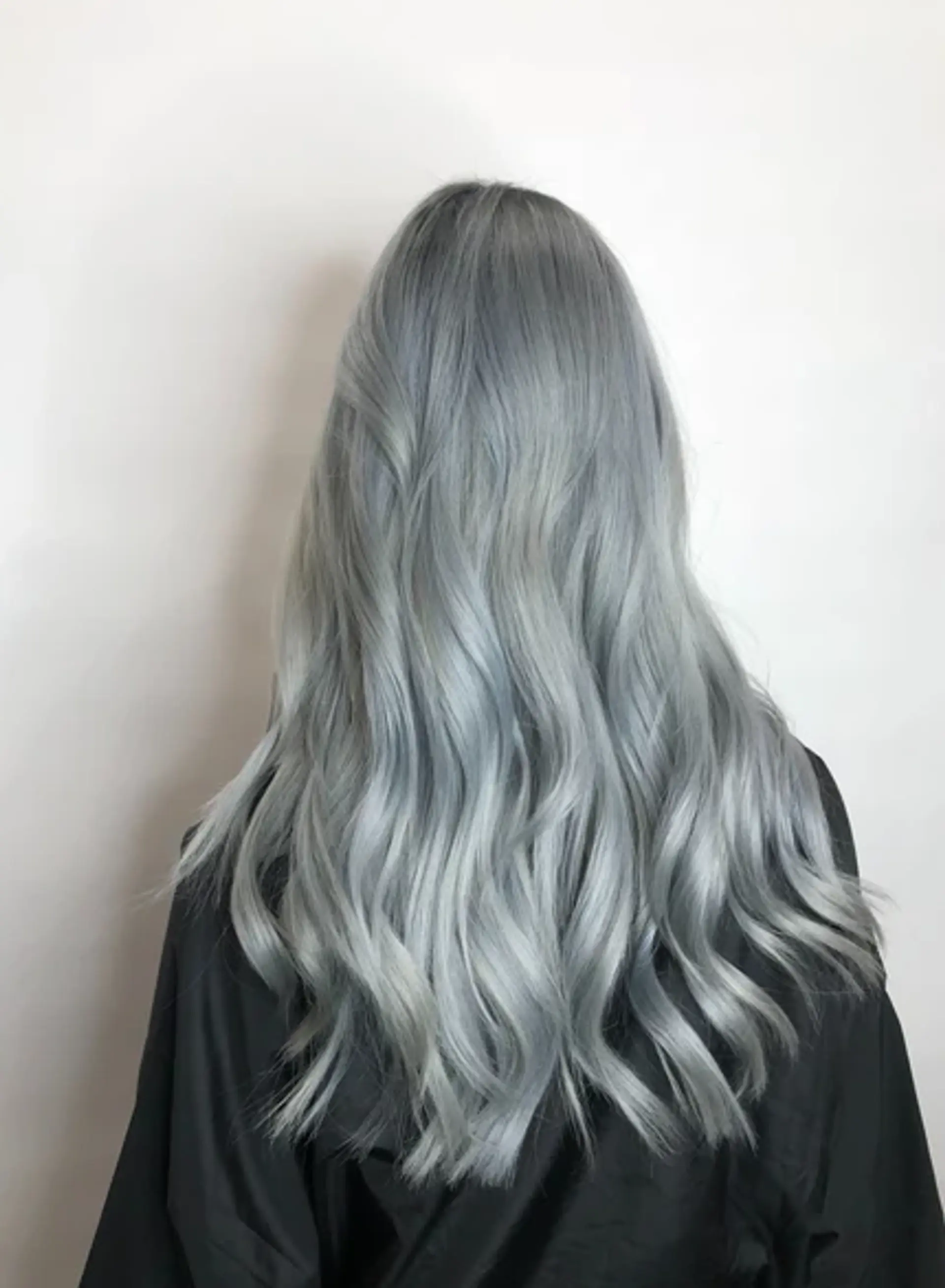 This sophisticated hairstyle features long, wavy locks colored in a striking silver-gray shade. The soft waves add volume and texture, with a smooth, shiny finish that enhances the dimensional color. 1