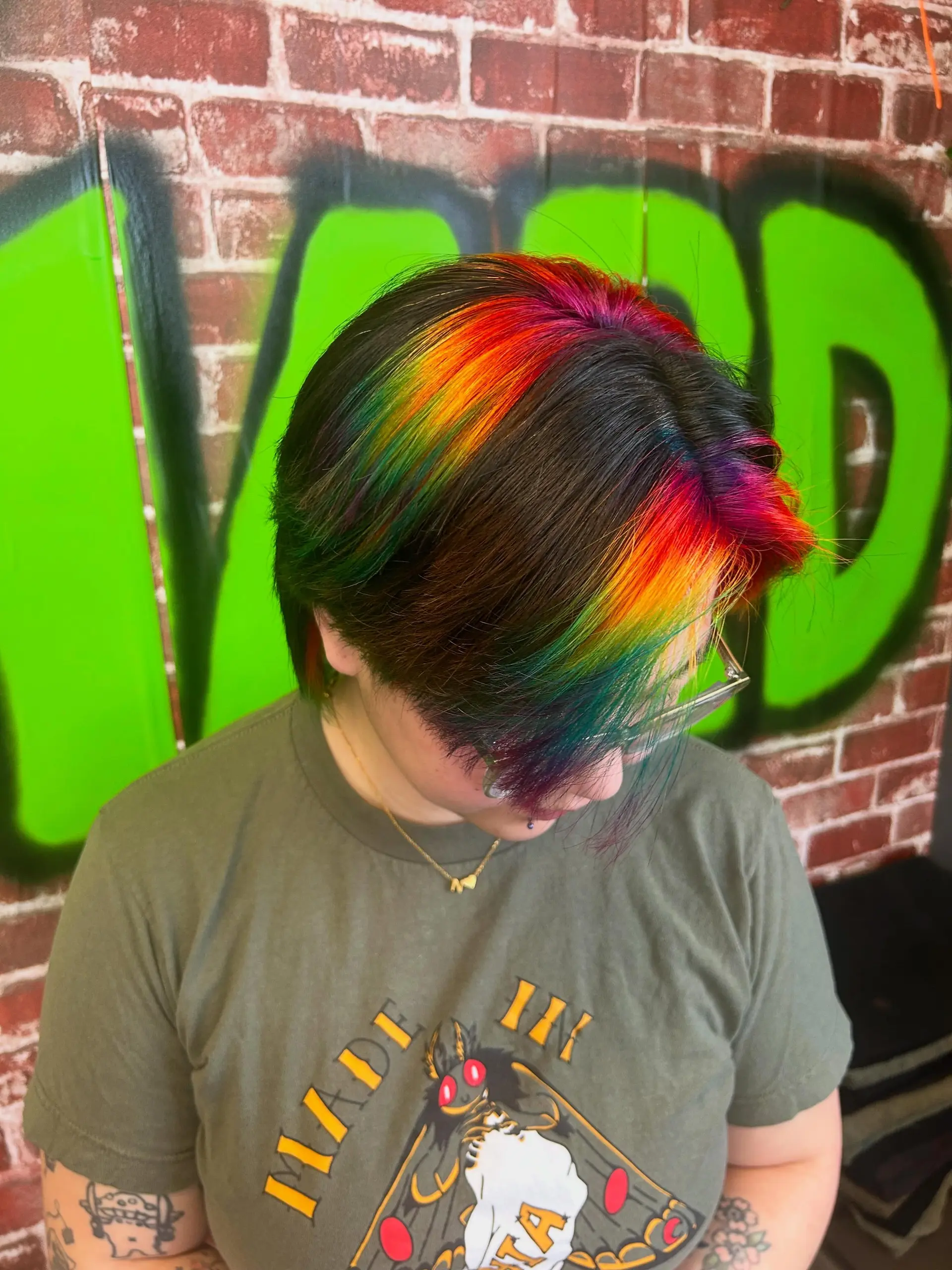 Short layered dark hair highlighted with vibrant rainbow vivid panels across the crown and fringe. 1