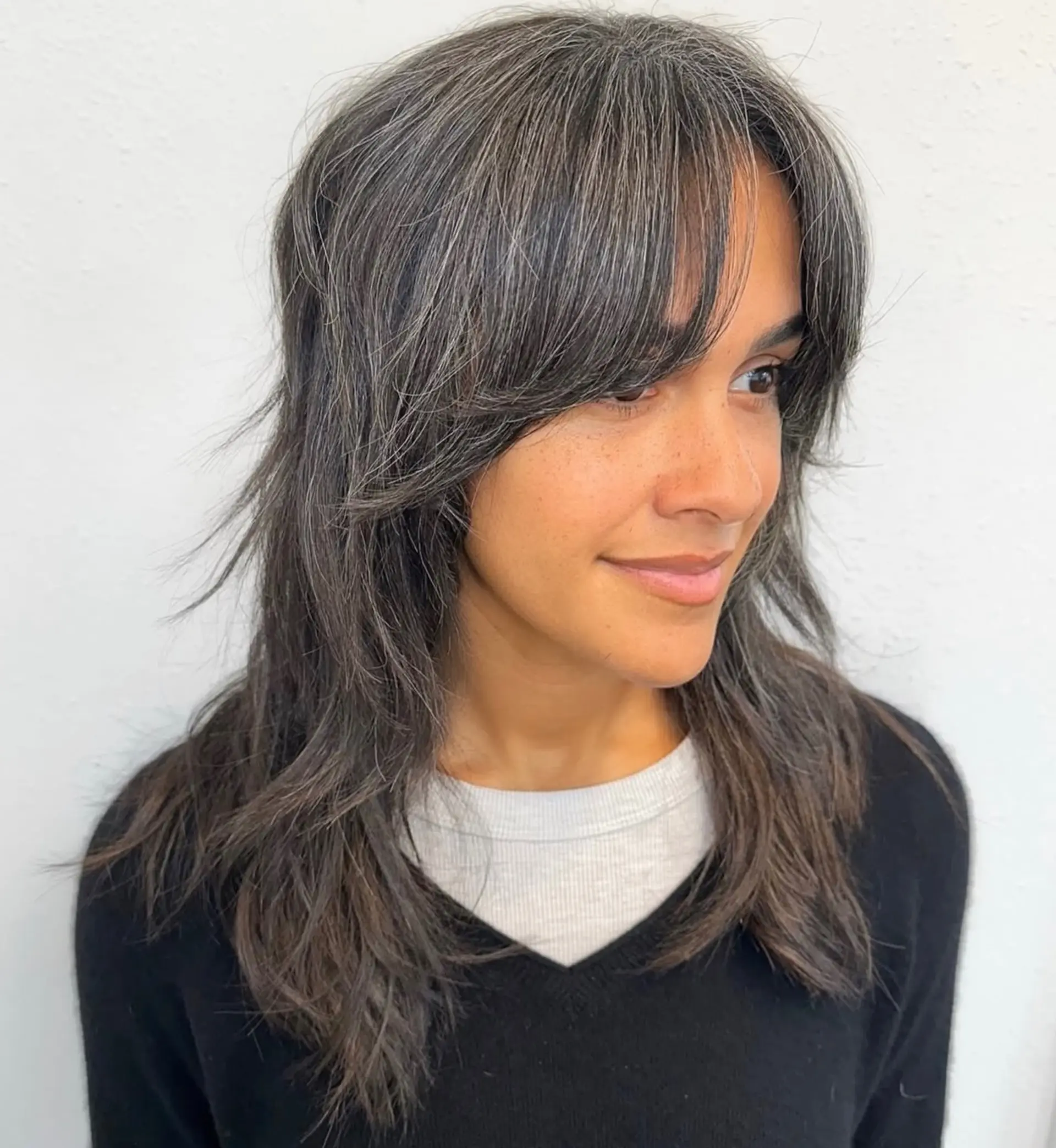 A medium-length textured shag haircut featuring feathered curtain bangs and soft, face-framing layers. 1