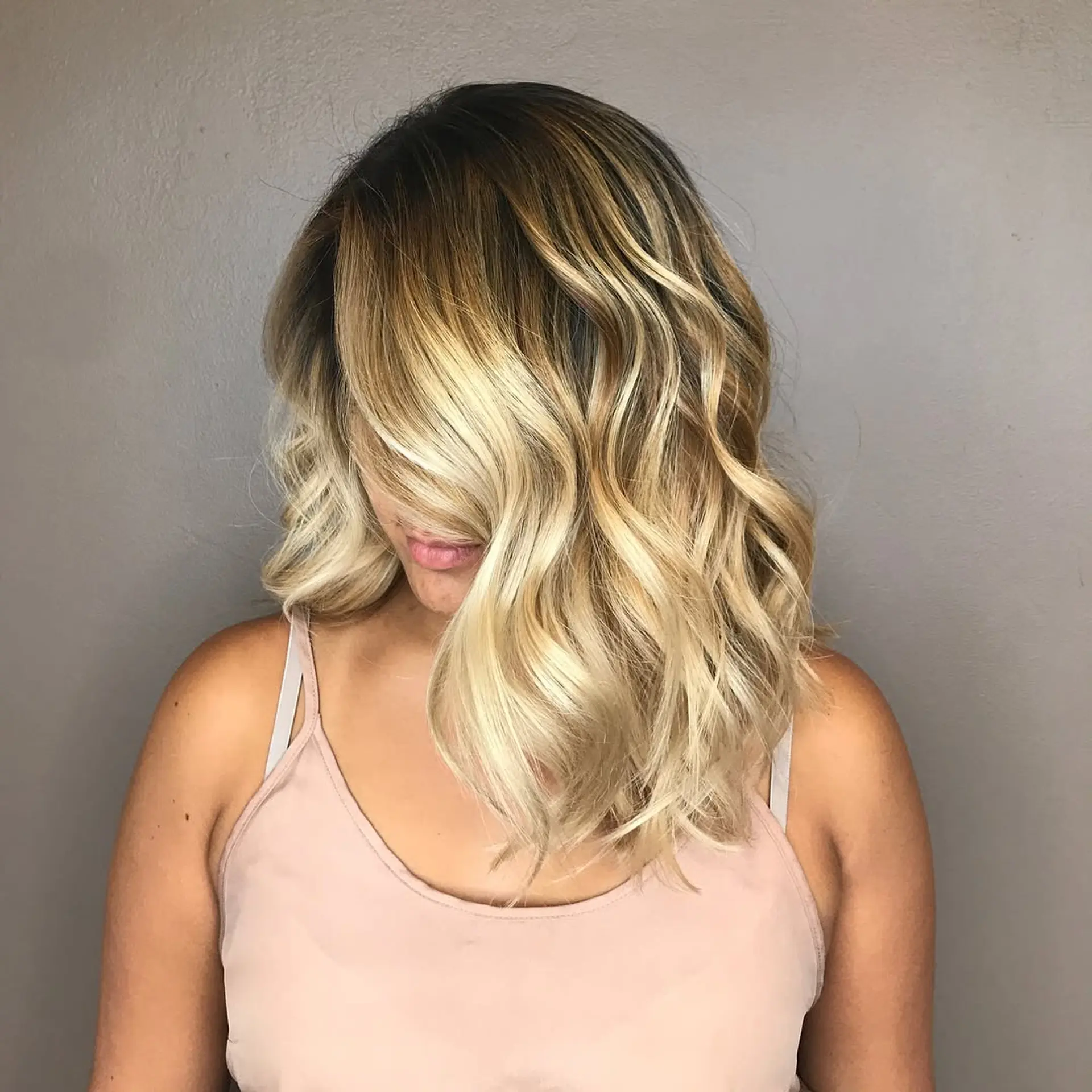 Shoulder-length textured lob styled in soft, loose waves featuring a seamless shadow root melting into bright golden blonde ribbons. 1