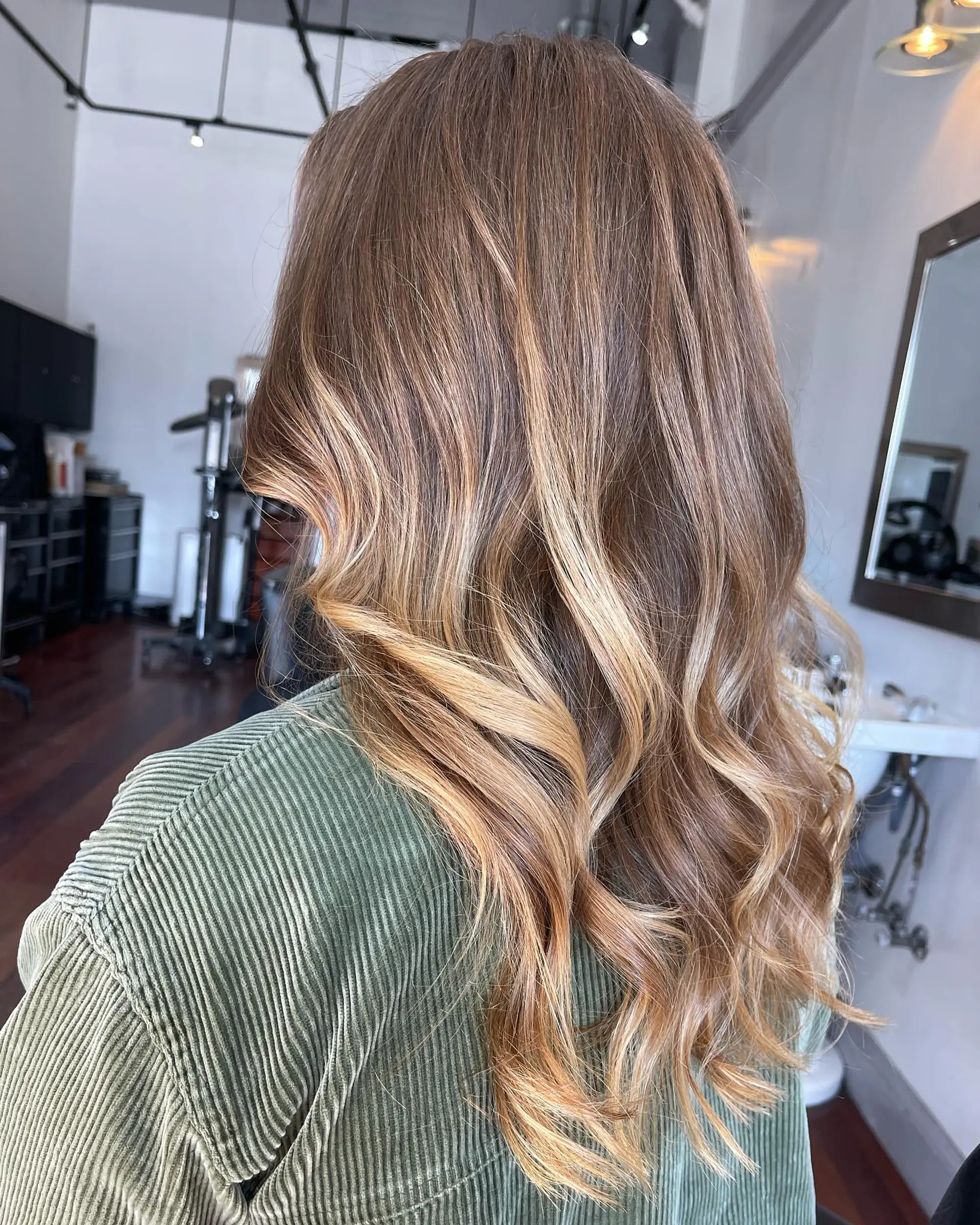Long dimensional caramel and golden blonde balayage styled in soft, glossy waves. 1