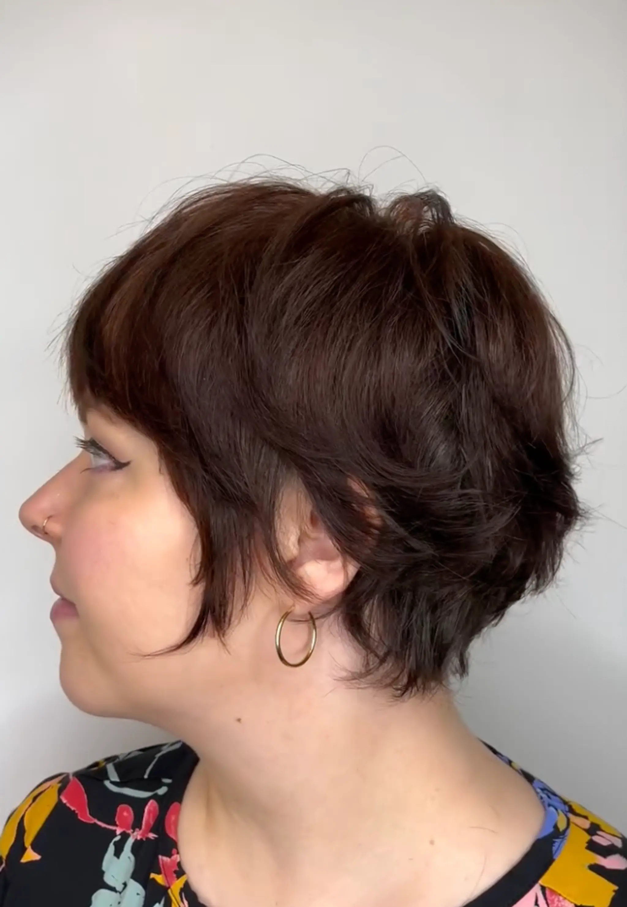 The hairstyle is a short, wavy, layered, mahogany-colored cut with voluminous texture and side-swept bangs, creating a chic, tousled look.

Cut and style by @juliamannino_hair


