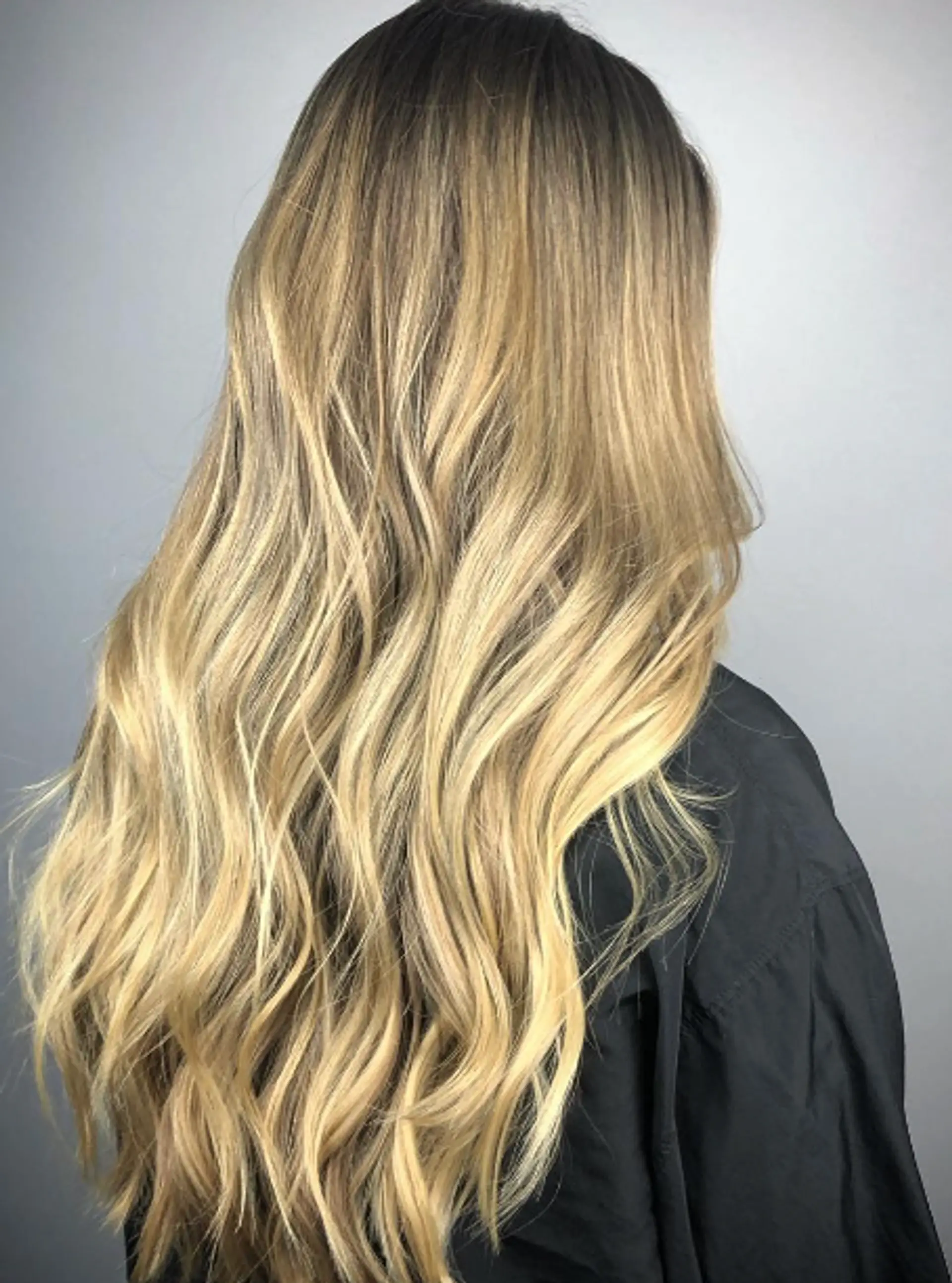 Very long, wavy hair with an ombre effect transitioning from dark blonde roots to golden blonde tips, featuring soft and natural waves and sun-kissed highlights. 1