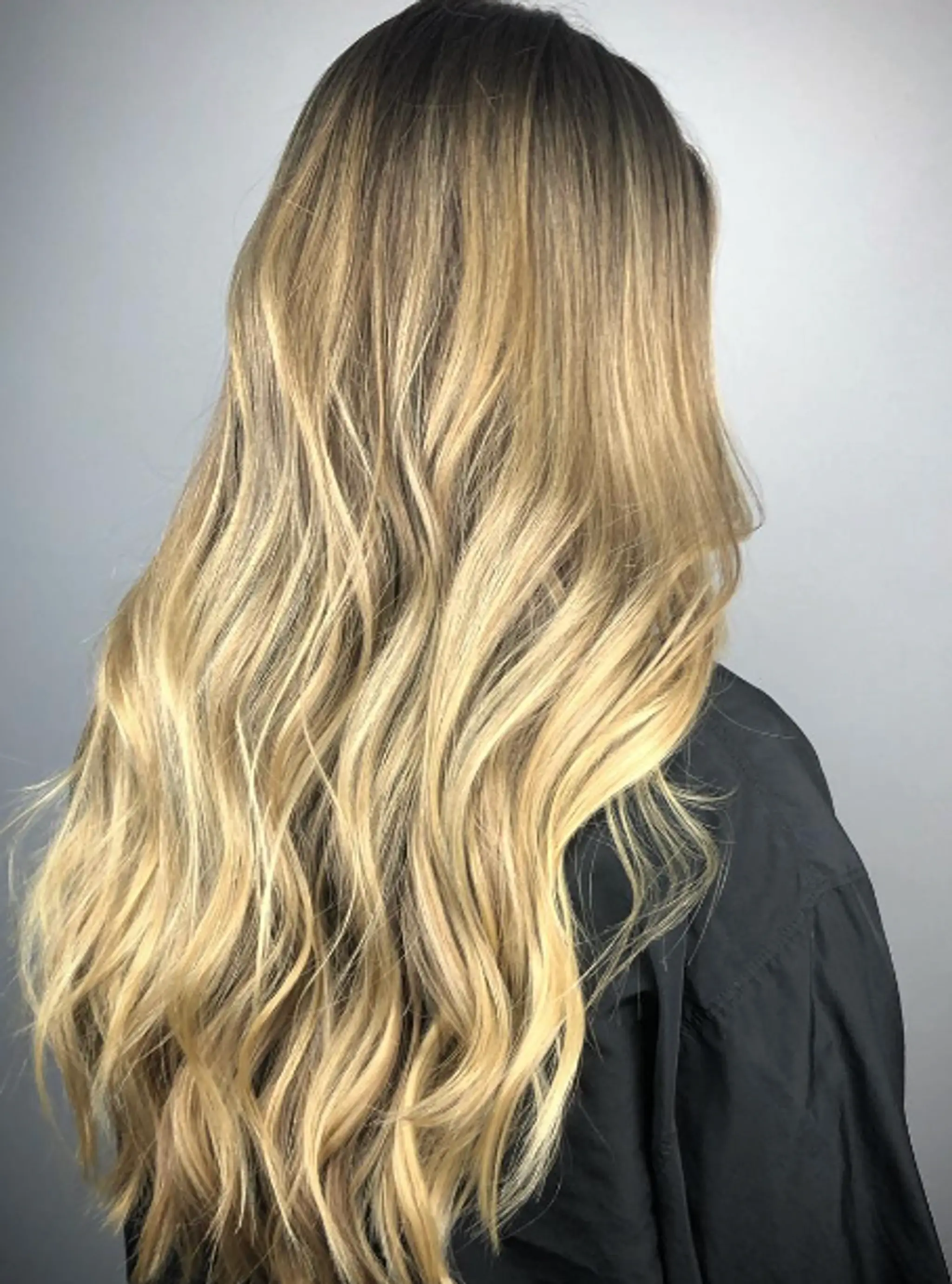 Very long, wavy hair with an ombre effect transitioning from dark blonde roots to golden blonde tips, featuring soft and natural waves and sun-kissed highlights.