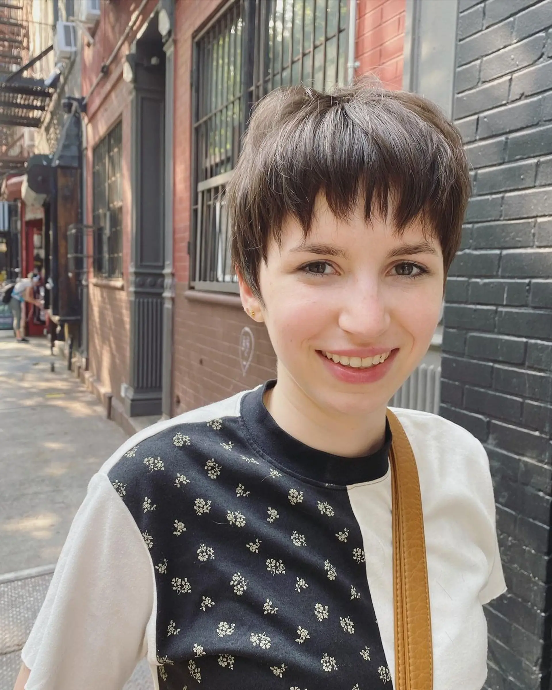 A short, textured pixie cut with choppy layers and fringe bangs in straight brown hair. 1