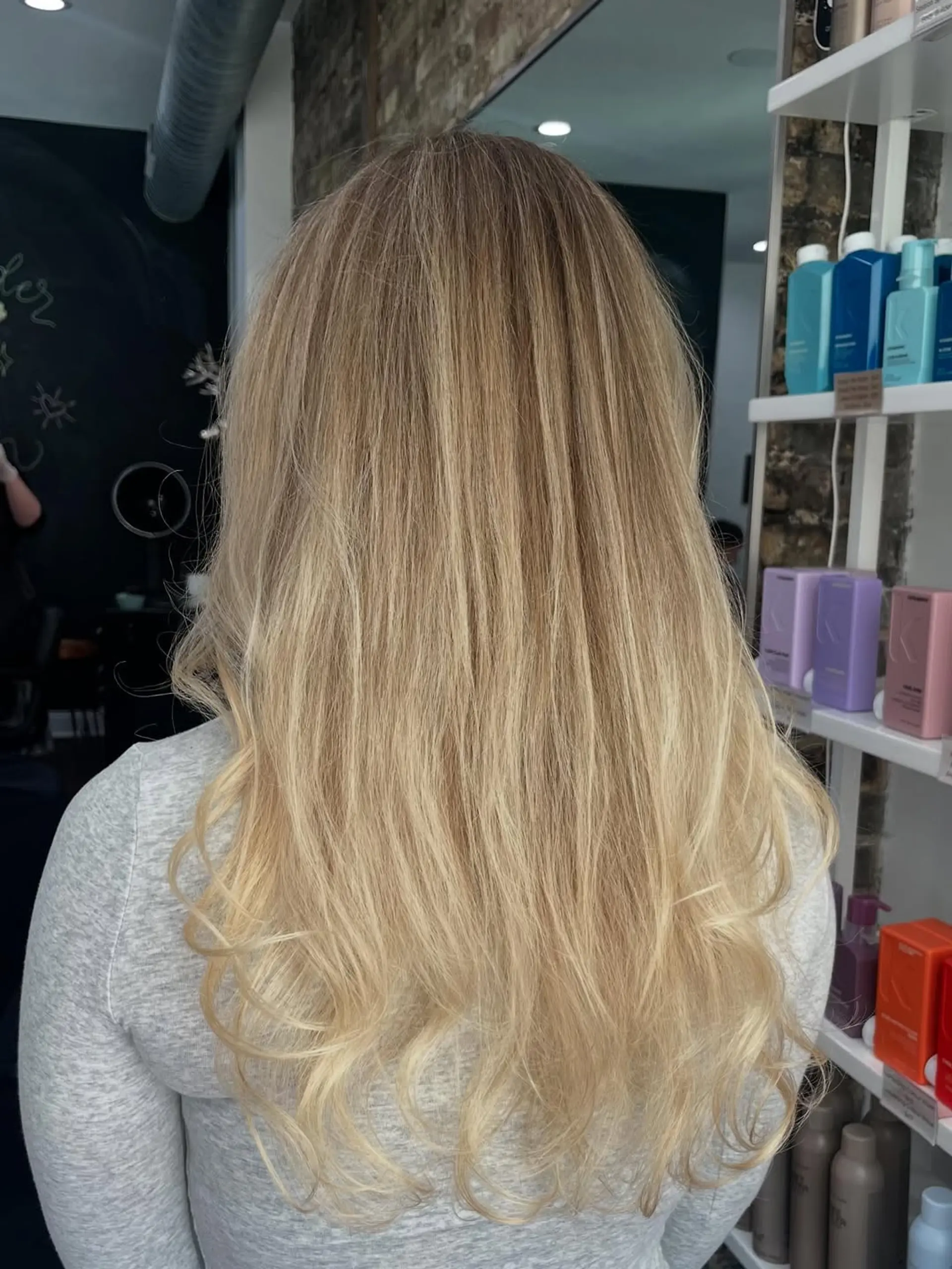 Long hair styled with soft, natural-looking waves, showcasing a dimensional blonde balayage. This style features seamless blending from slightly darker roots to brighter, multi-tonal blonde ends. 1