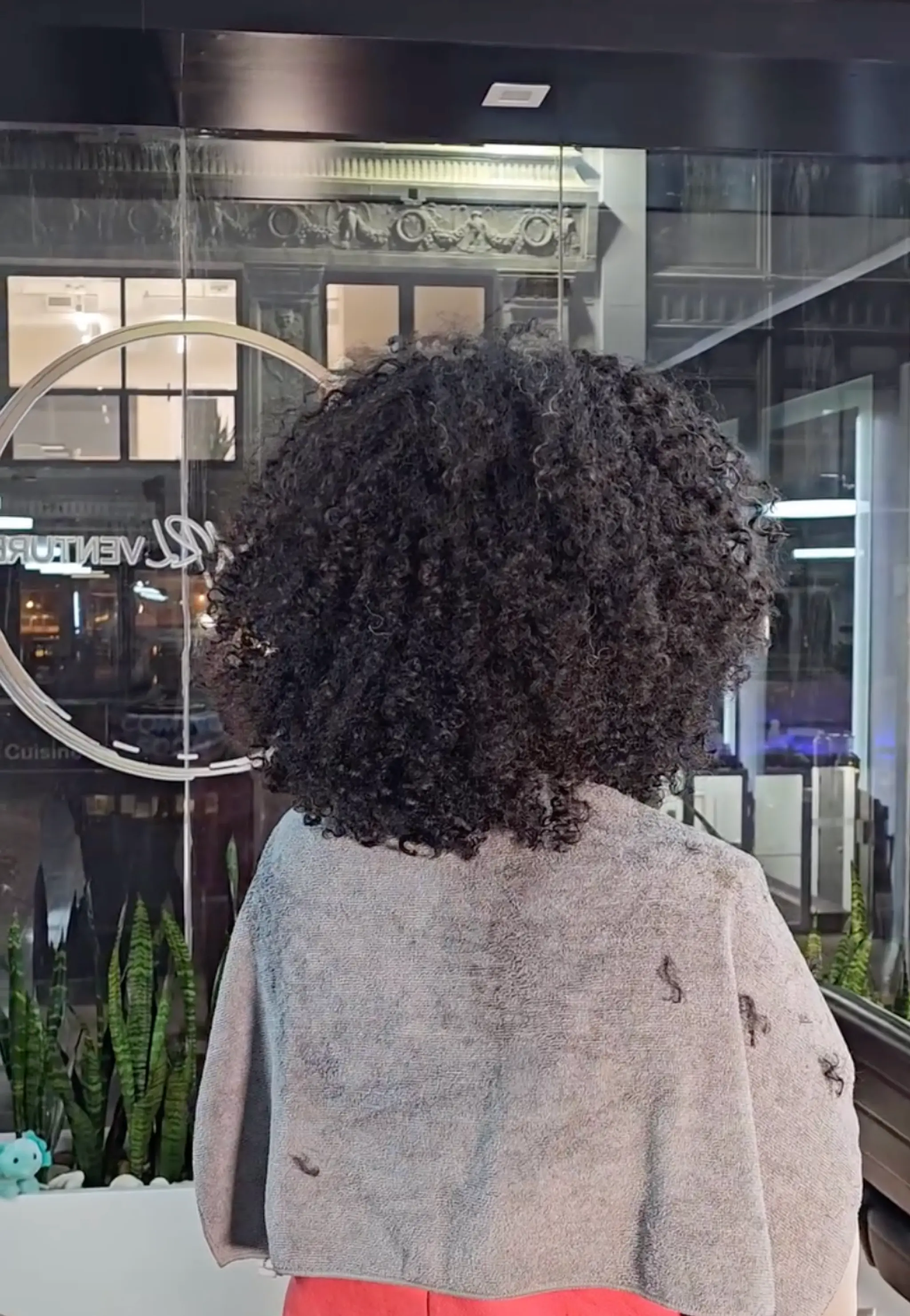 Medium-length dense, natural curls with high volume and a round shape, black in color, reaching just above the shoulders.