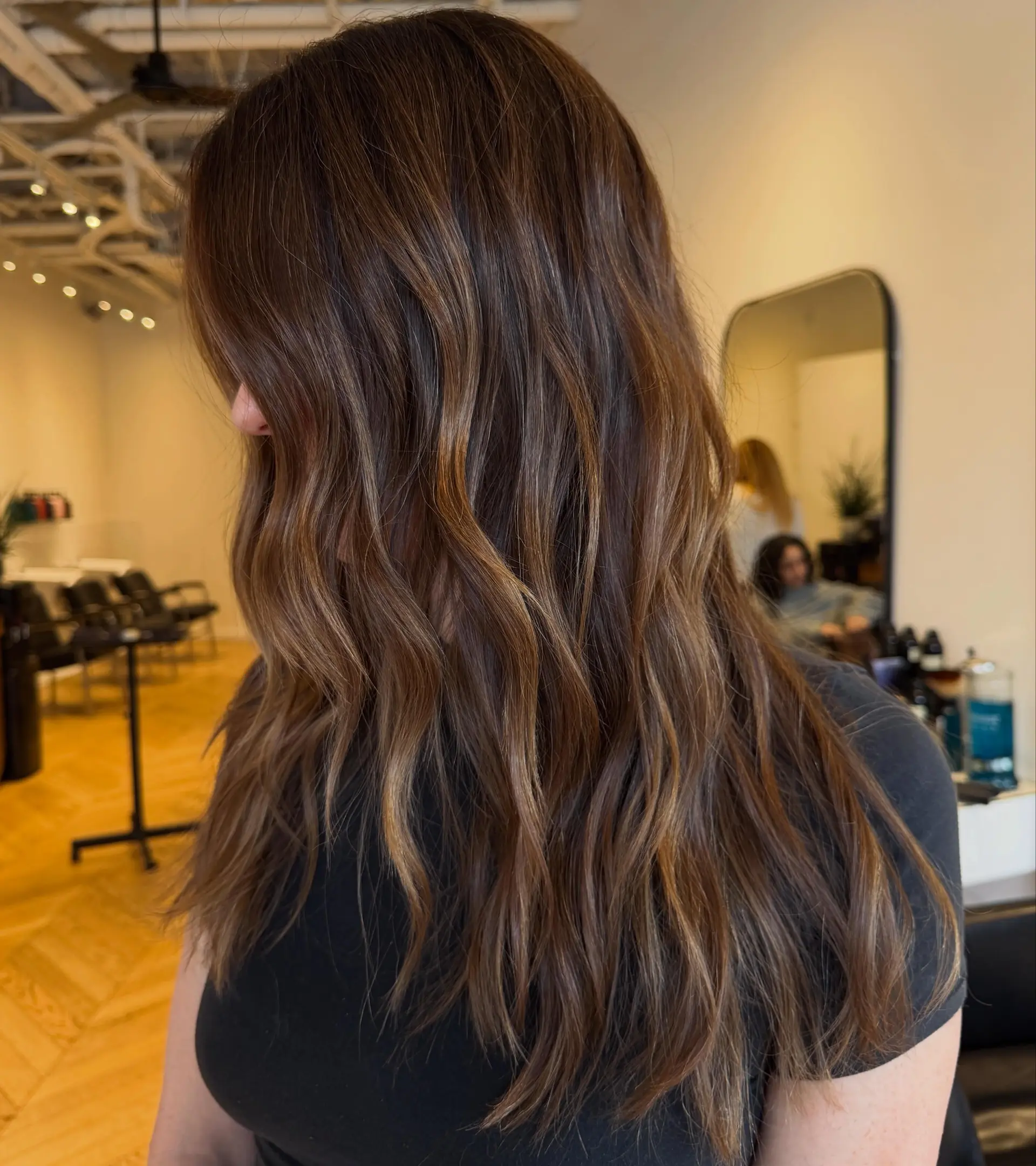 Long dark brown hair featuring fine warm caramel highlights styled in soft loose waves. 1