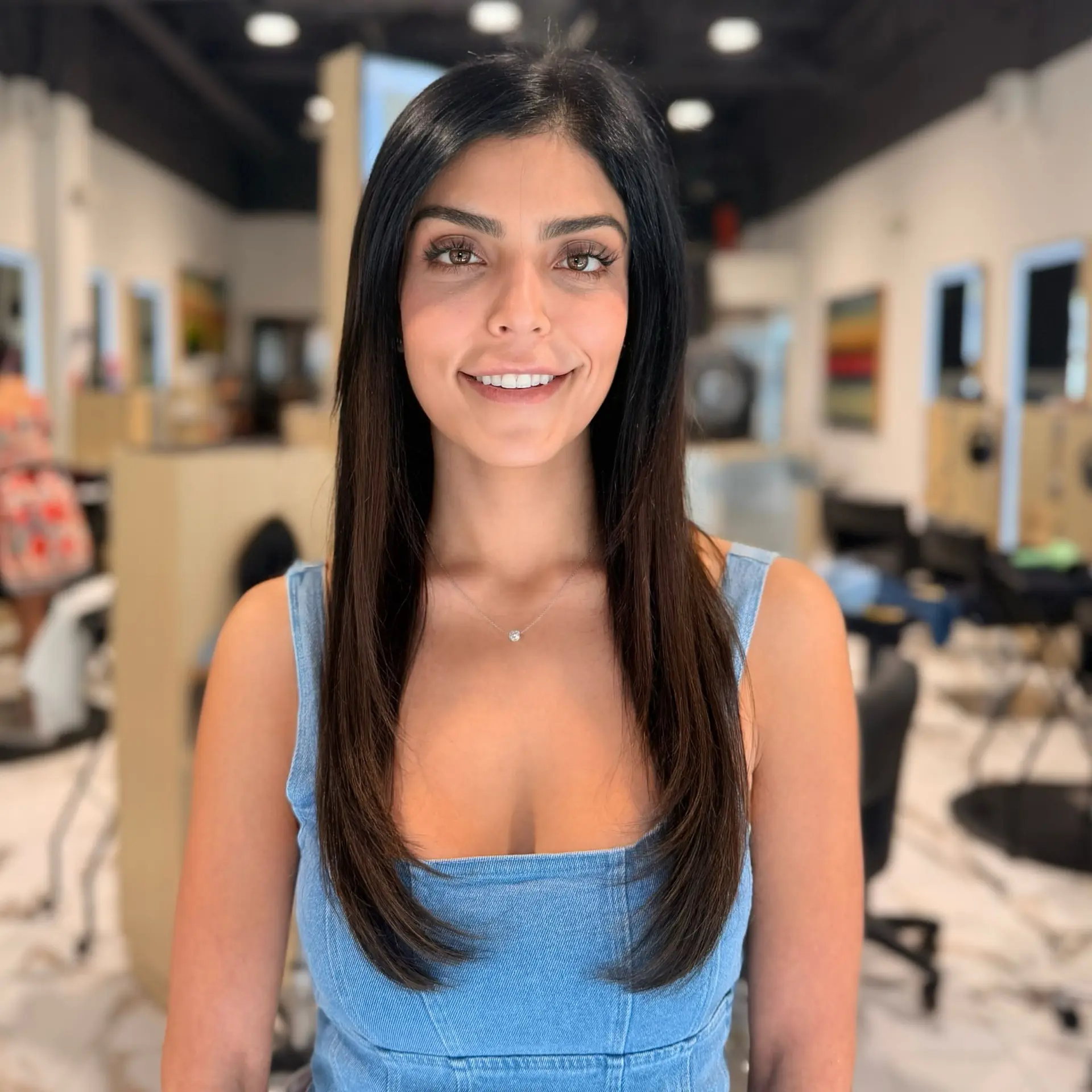 Long, glossy dark brunette hair seamlessly blended with extensions, styled sleek and straight with subtle inward beveling at the ends. 1