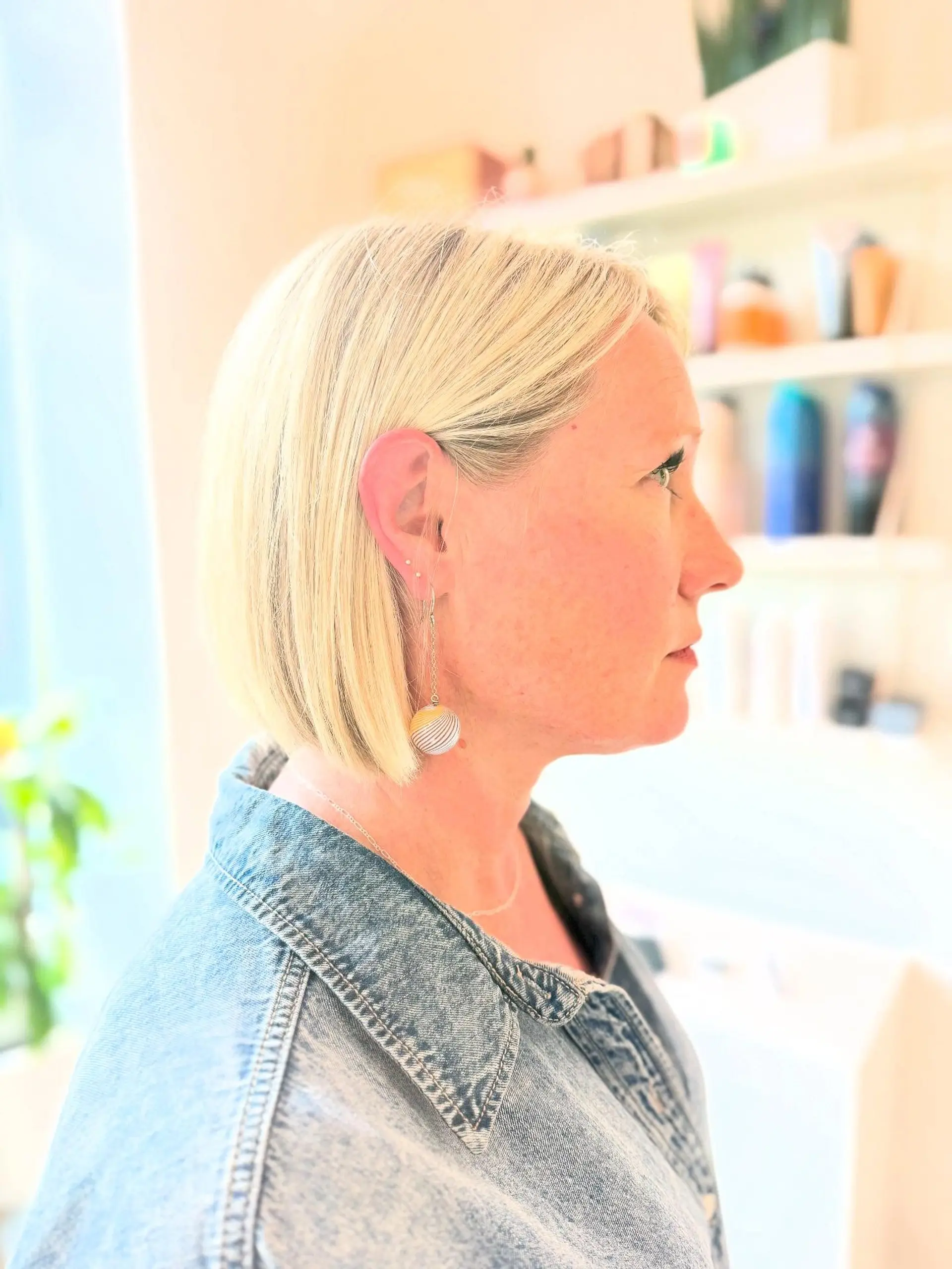 A sleek, chin-length blunt blonde bob with straight styling, tucked gently behind the ear. 1