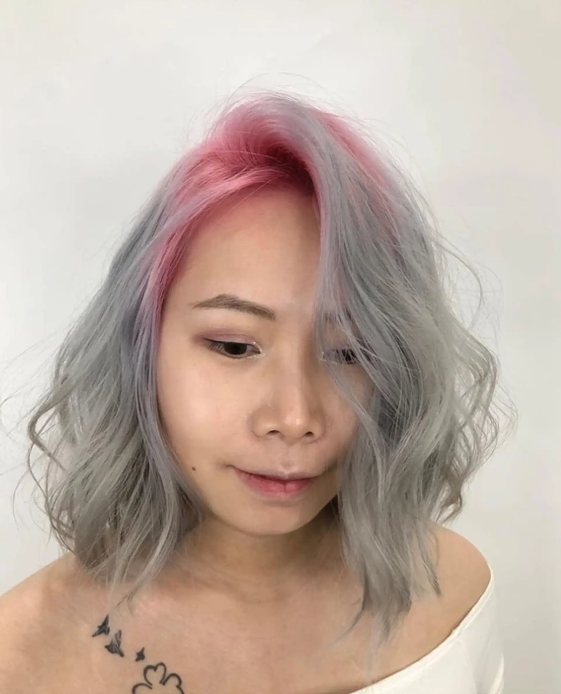 Medium-length wavy hair styled into loose, soft curls with a two-tone color scheme of pink at the roots transitioning to silver along the lengths, featuring a modern, tousled bob cut. 1