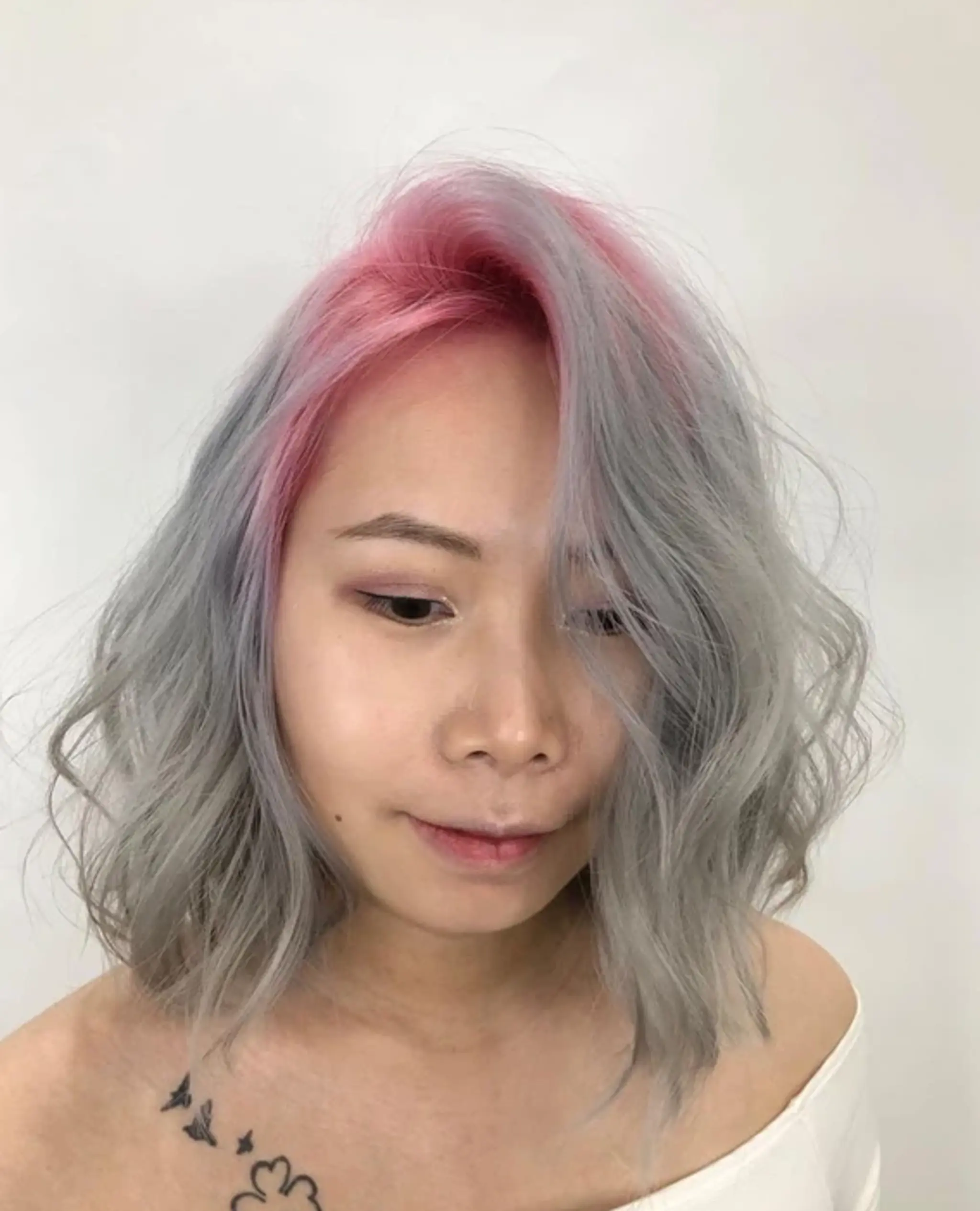 Medium-length wavy hair styled into loose, soft curls with a two-tone color scheme of pink at the roots transitioning to silver along the lengths, featuring a modern, tousled bob cut.