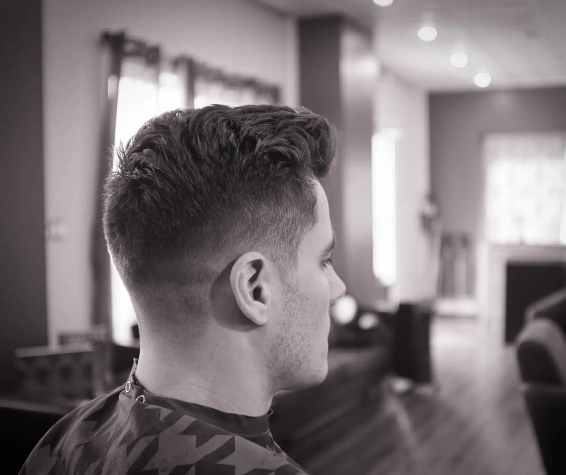 A clean mid taper fade with short blended sides and a textured, styled top. 1