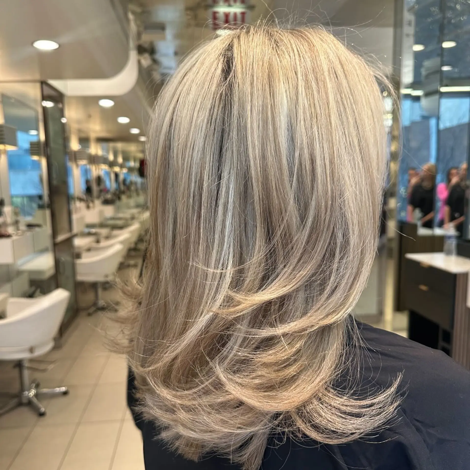 Medium-length cool ash blonde hair cut with flowing, feathered layers and styled with flicked ends. 1