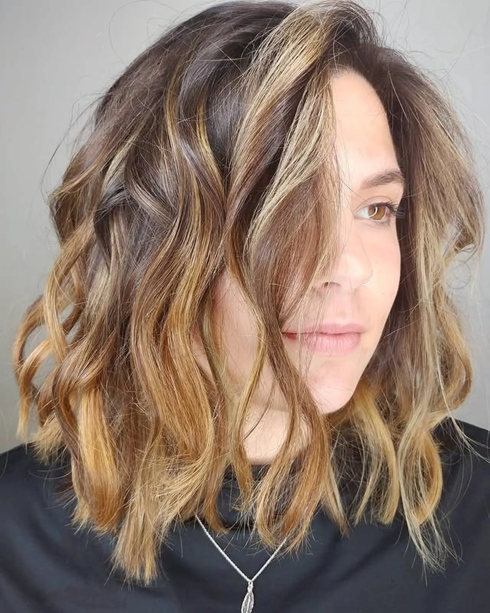 A medium length wavy hairstyle with a seamless blend of brown and blonde tones in a balayage technique, creating a soft, dimensional look. 1