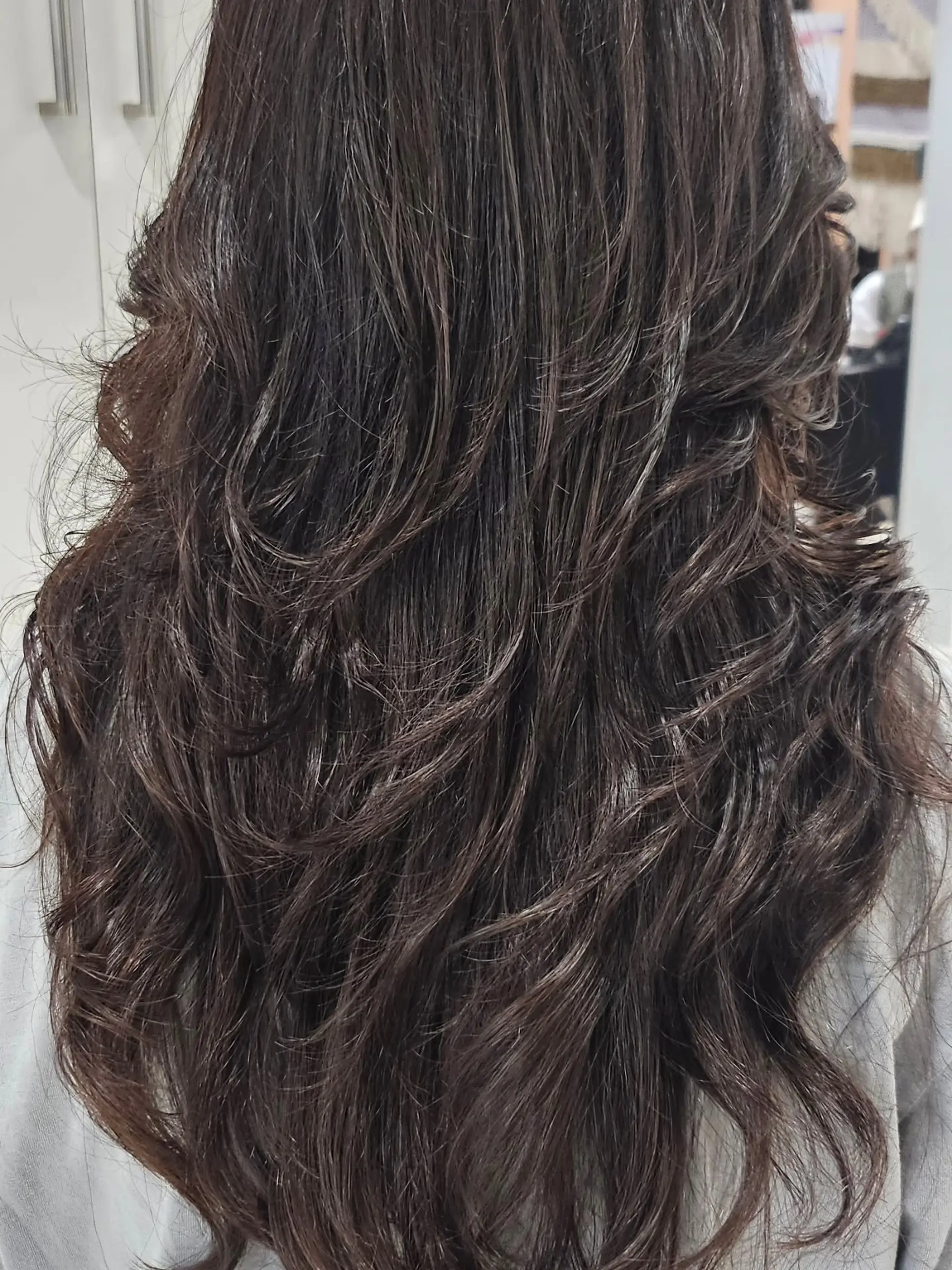 Long dark hair cut in flowing layers with soft, dimensional digital perm waves that provide natural texture and movement. 1