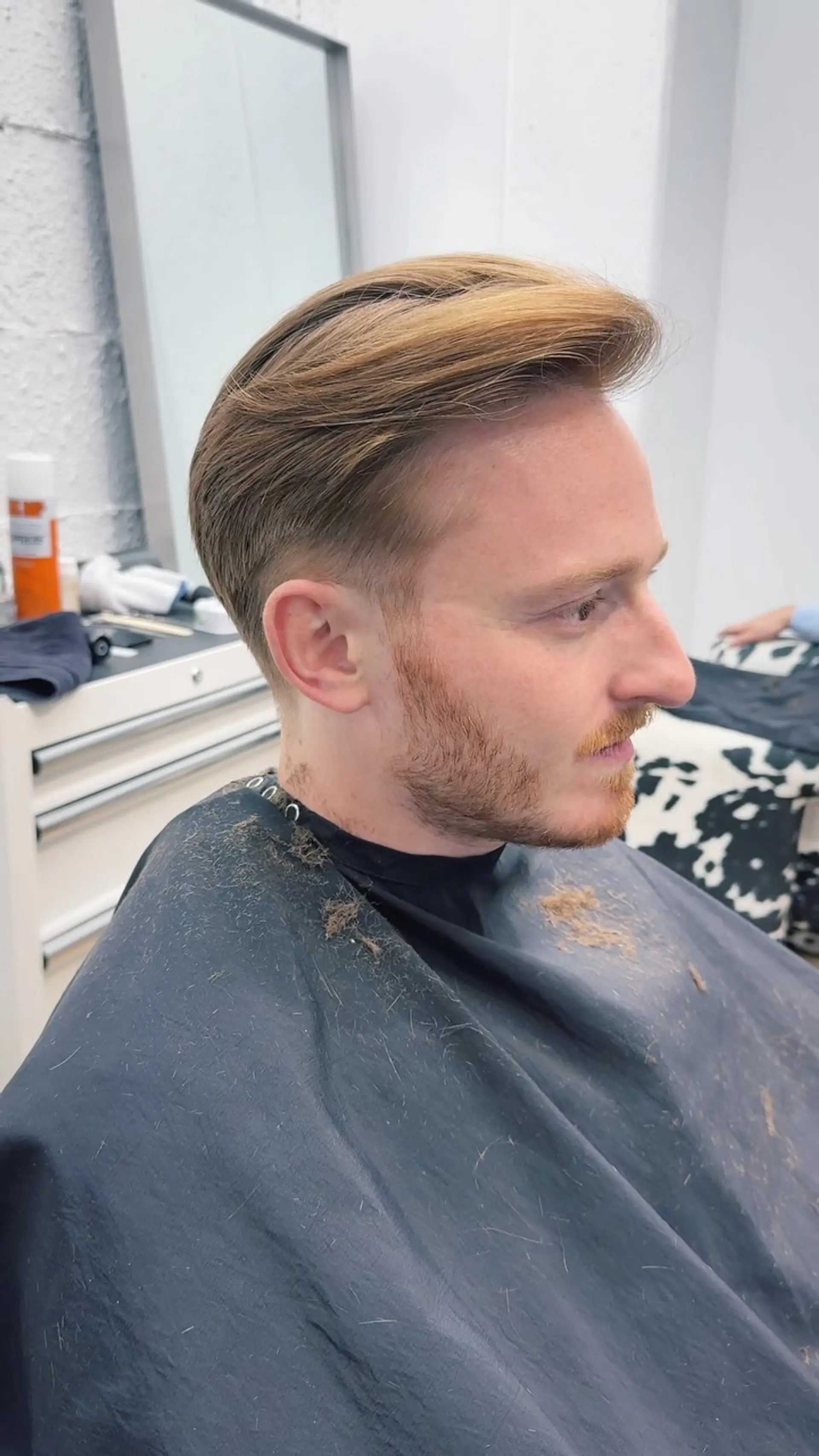 A refined men's haircut with length maintained and brushed back on top, paired with a soft taper around the ears and neckline. 1