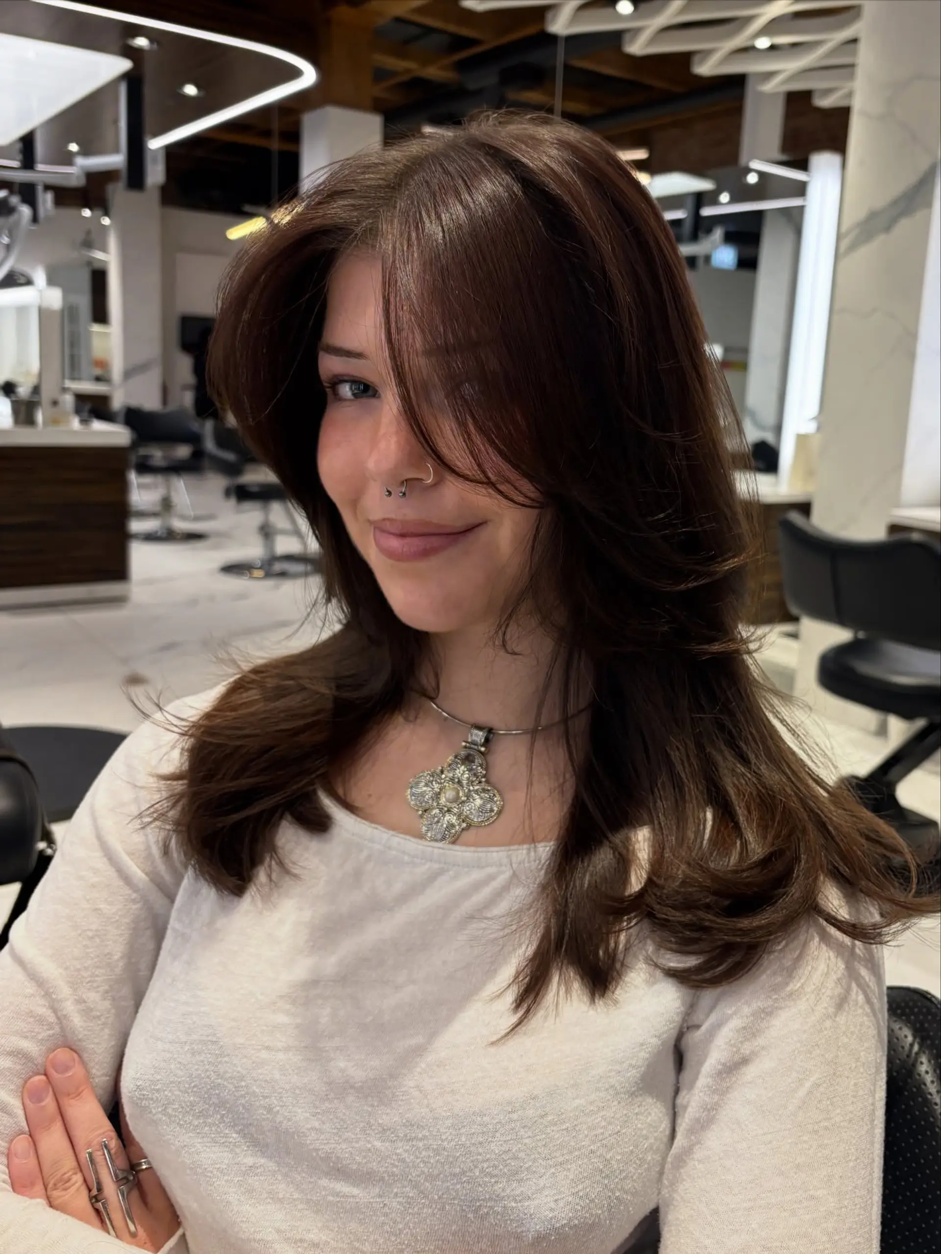 A rich chocolate brown haircut featuring long flowing layers, soft face-framing curtain bangs, and a voluminous blowout finish with gentle curved ends. 1