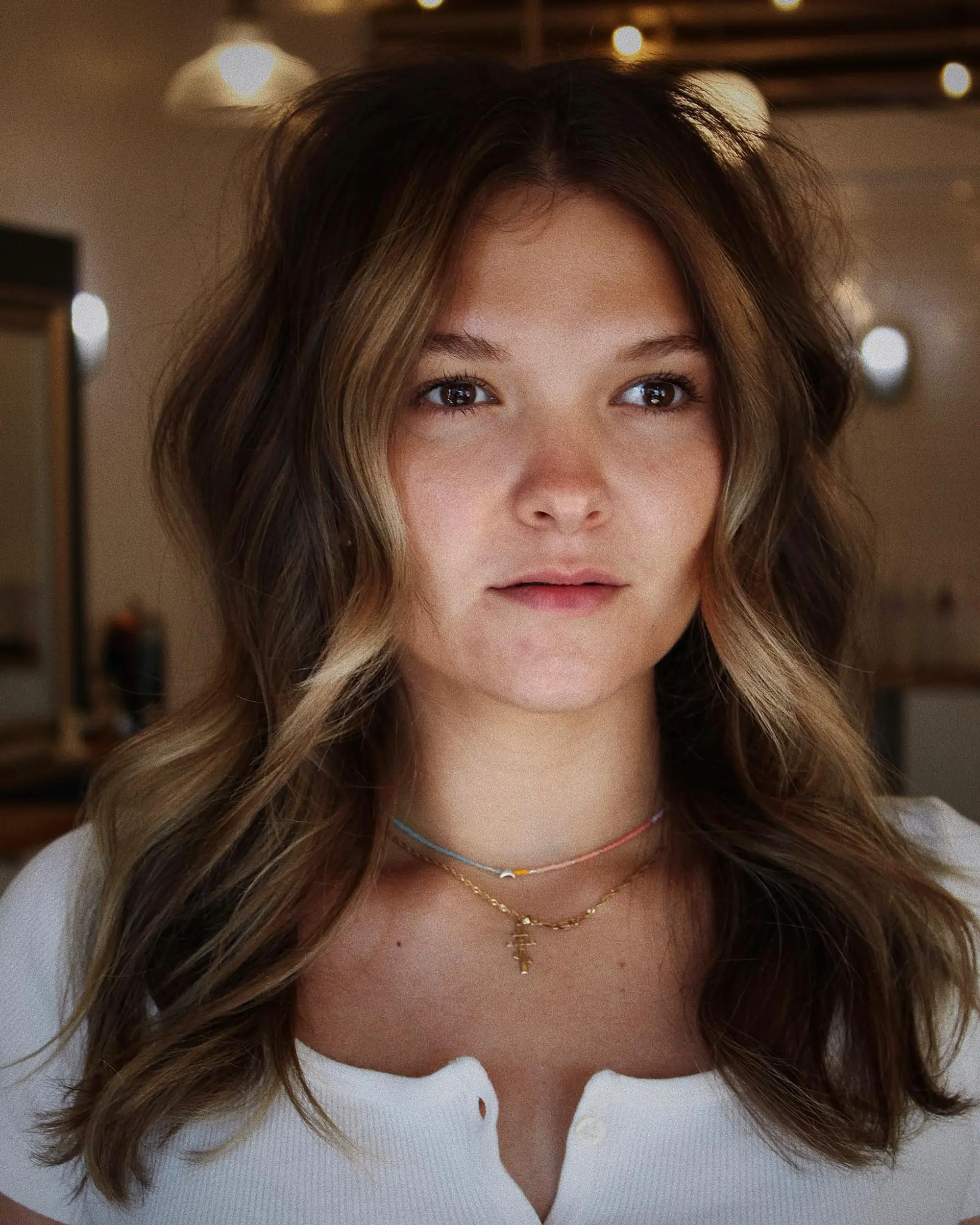 Medium-to-long wavy brunette hair with soft, face-framing dimensional balayage highlights and a middle part. 1