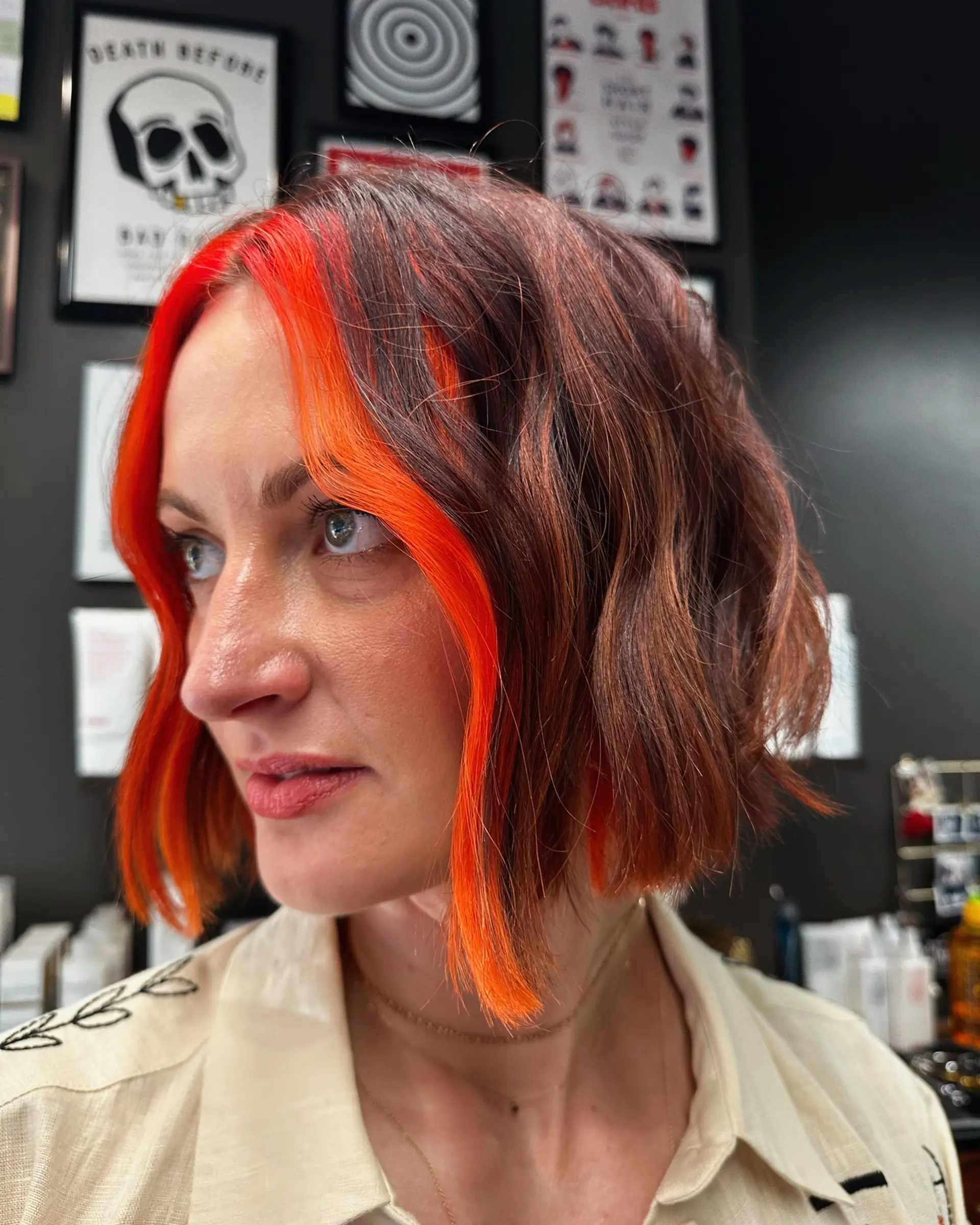 Chin-length textured wavy bob featuring a striking, vibrant neon orange money piece framing the face against a warm auburn-brown base. 1