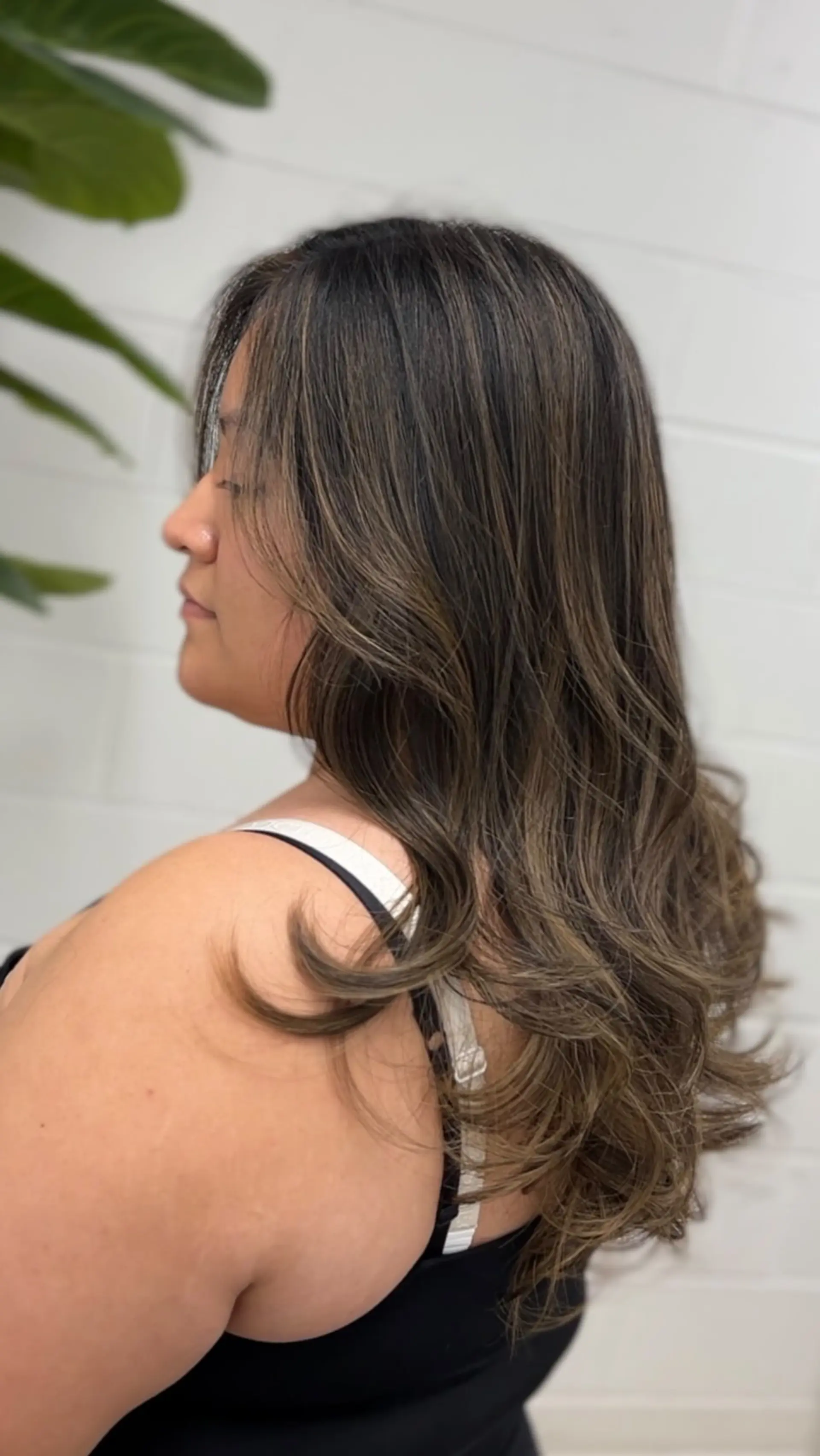 Long dark brown hair enhanced with seamless ash brown foilayage highlights and styled into soft, voluminous waves. 1