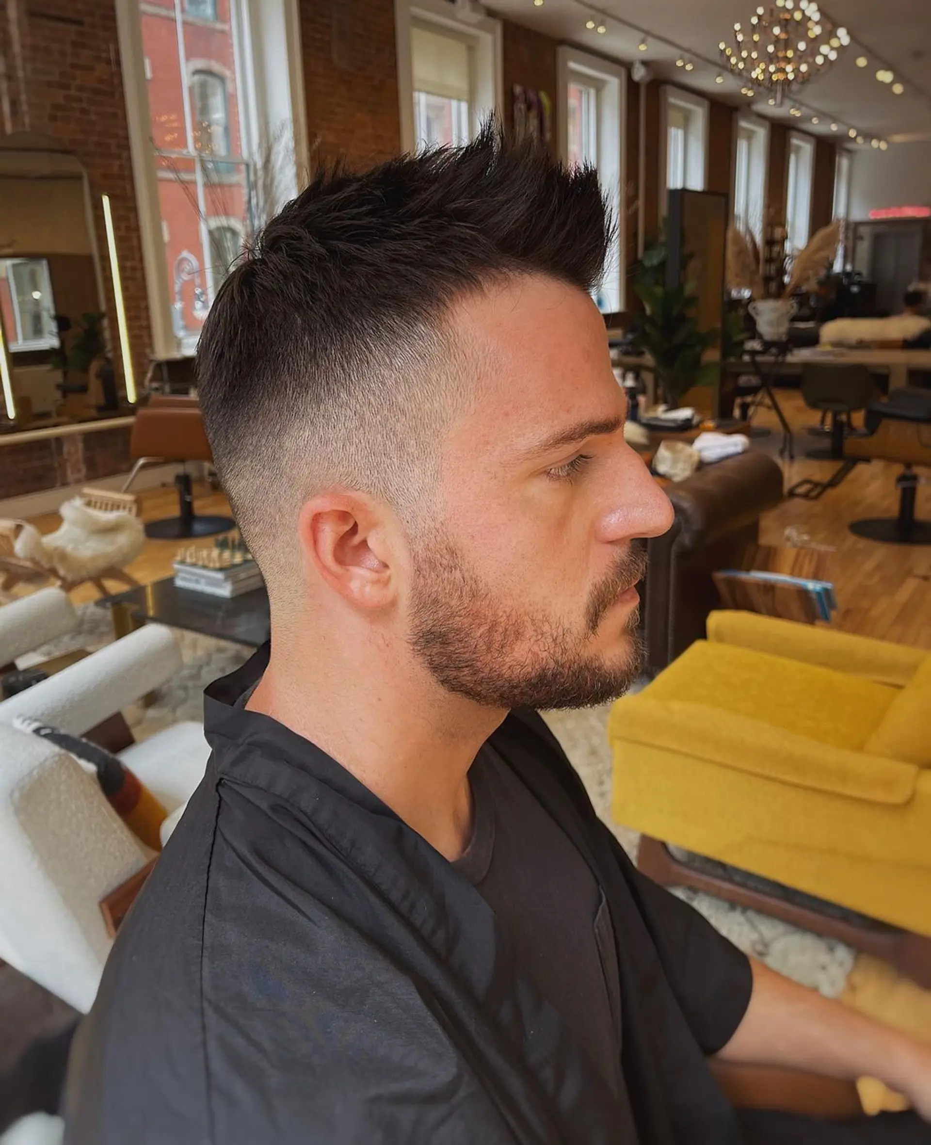 High fade with a textured and spiky top, clean lines, and a side part, complemented by a neatly trimmed beard. 1