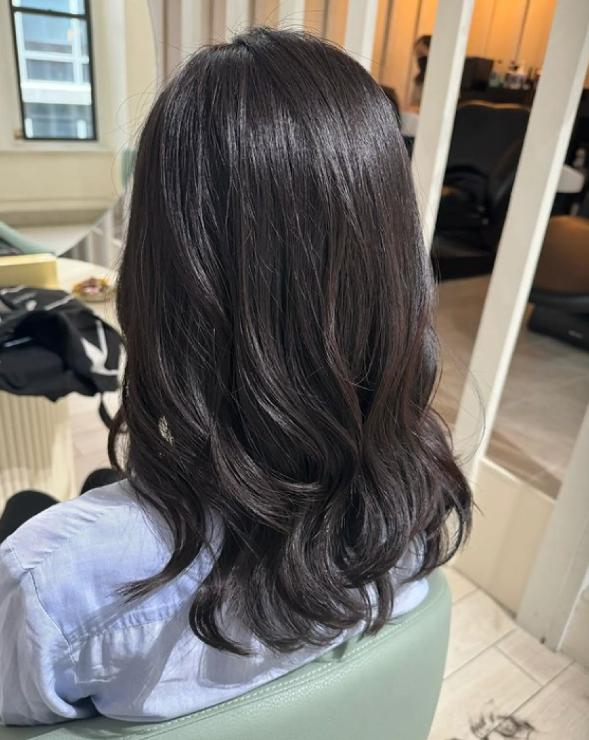 Medium-length, dark brown to black wavy hair with a glossy finish, featuring soft waves and layered styling.

