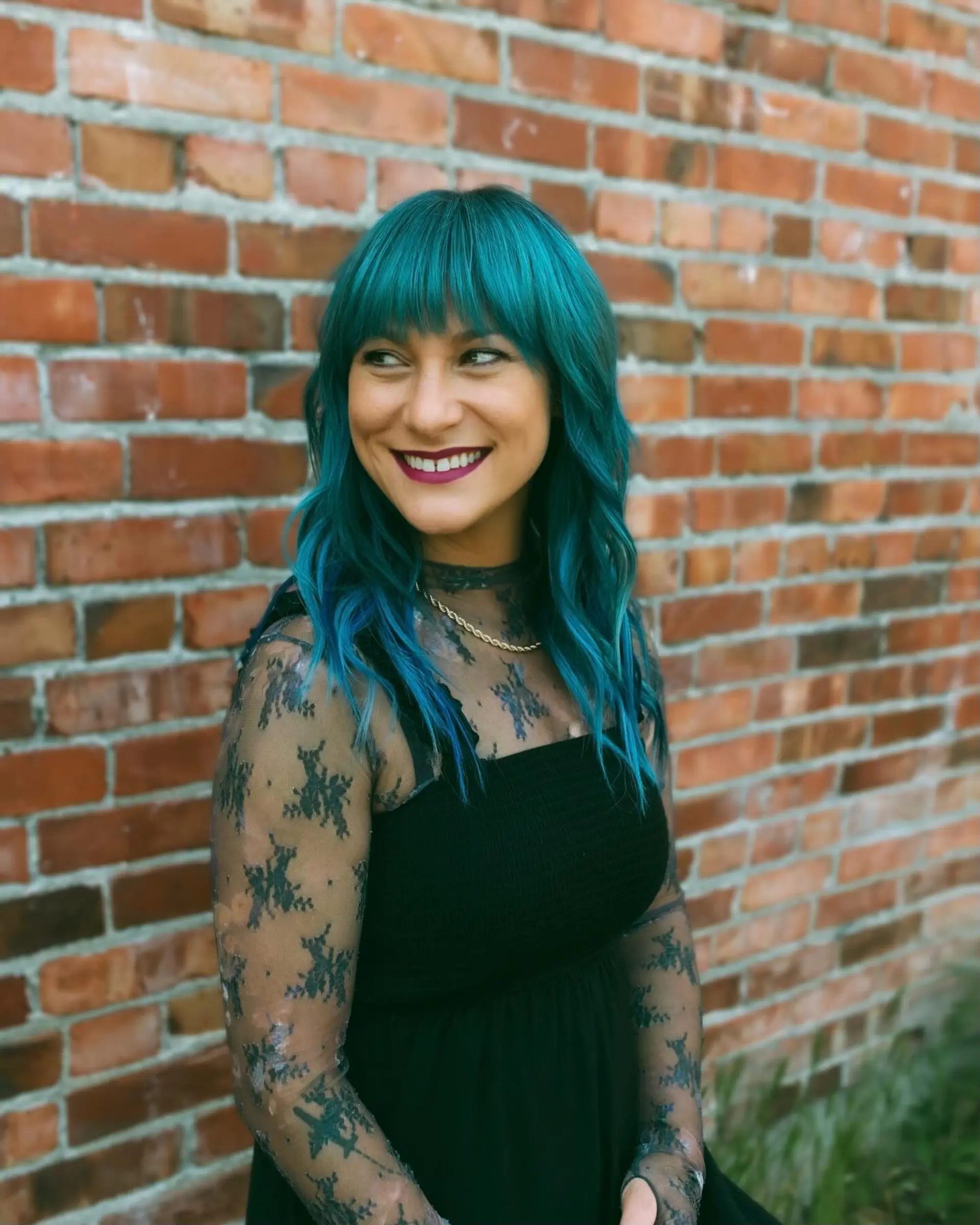 Medium-length layered cut dyed in a vibrant teal-blue hue, styled with soft beachy waves and a full straight-across fringe. 1