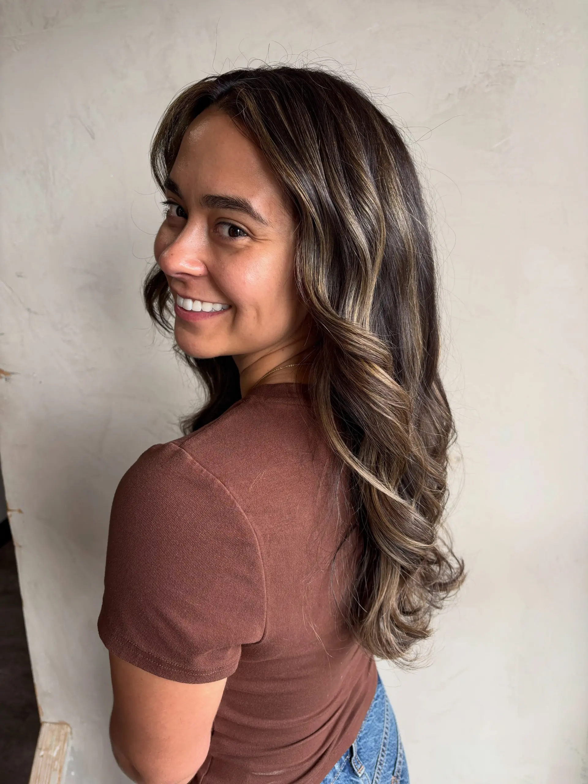 Long dark brunette hair styled with soft, loose waves and multi-dimensional caramel blonde balayage highlights. 1