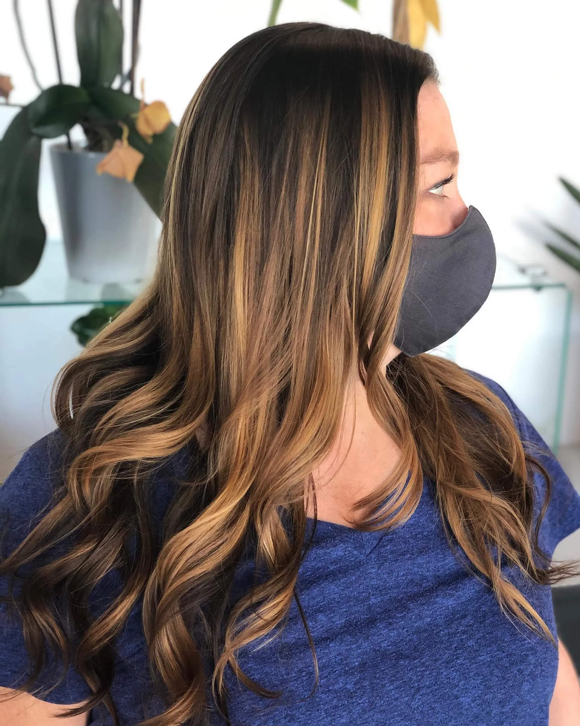 Long dark brown hair highlighted with warm caramel balayage and styled into loose, bouncy curls. 1