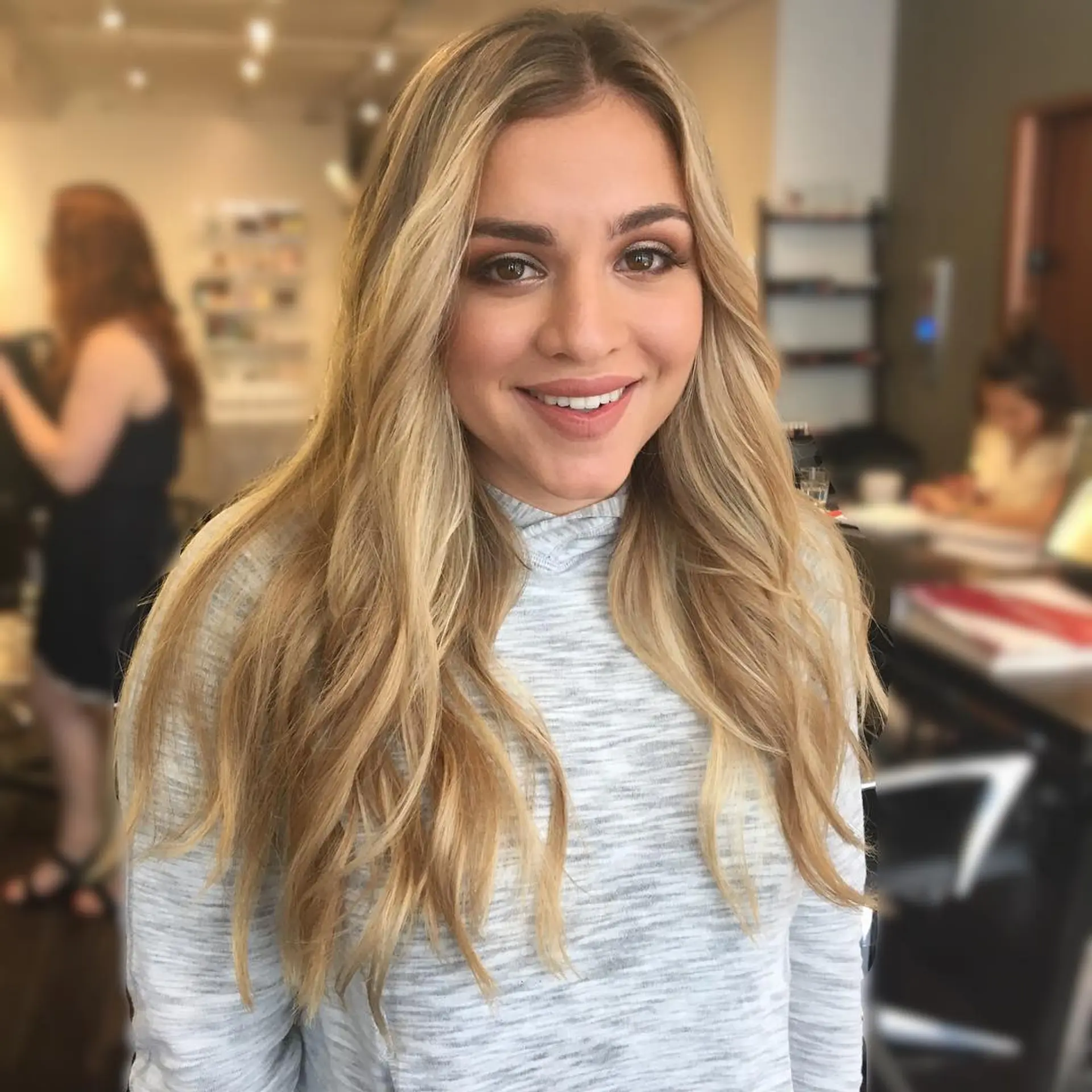 Long multi-dimensional blonde hair styled into soft, lived-in beach waves with a center part. 1