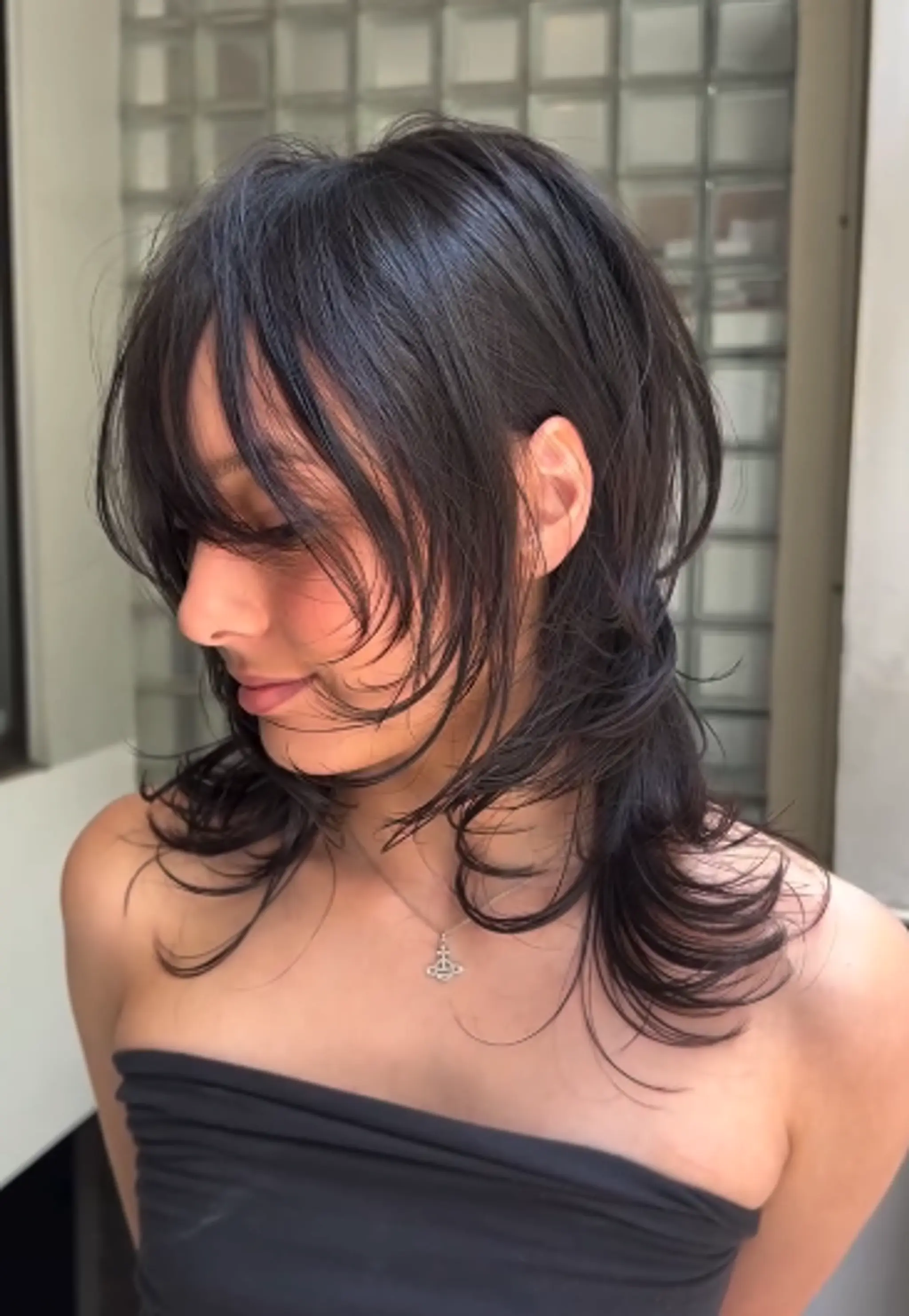 A medium length, dark brown hairstyle with wavy, feathered layers that gently frame the face, featuring textured ends and a breezy, soft flow. 1