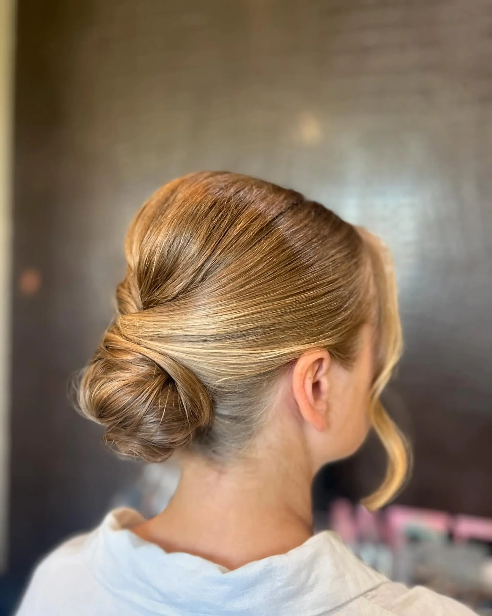A sleek, elegant low chignon updo pinned at the nape of the neck with soft face-framing pieces. 1