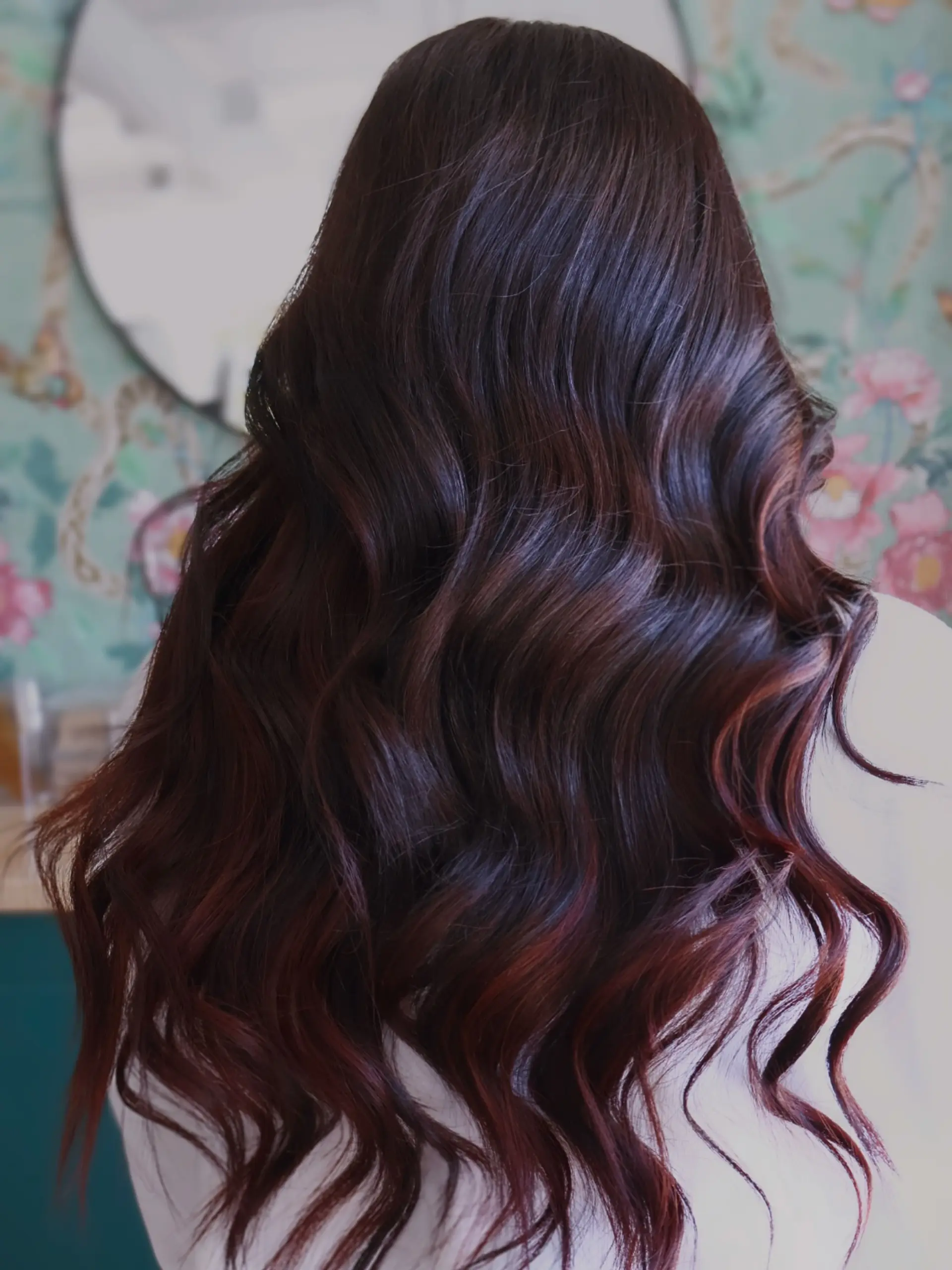 Long, flowing dark hair with deep auburn and burgundy tones styled into soft, glossy barrel waves. 1