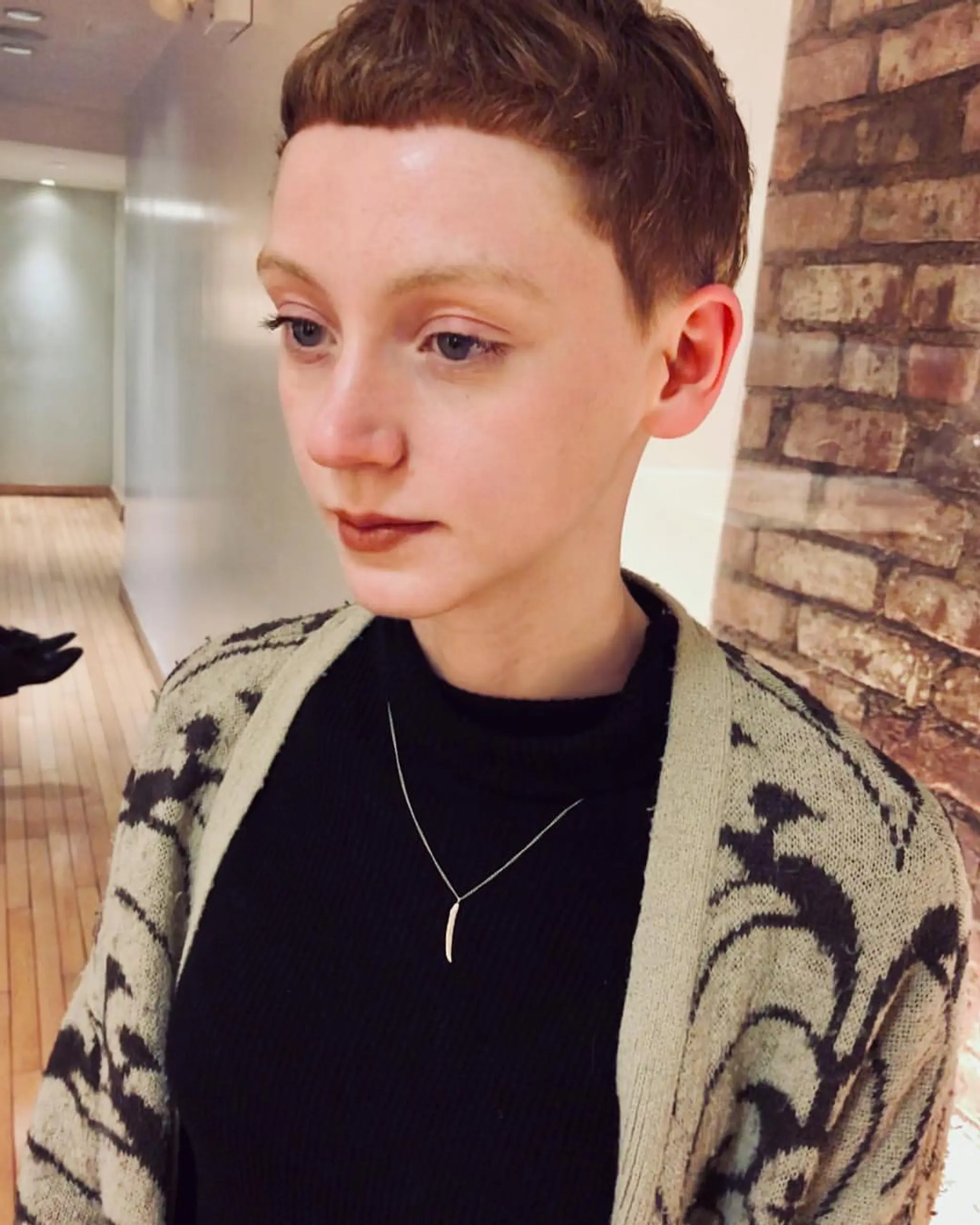 A very short auburn pixie cut with blunt micro bangs, tapered sides, and a defined hairline for a retro appearance. 2