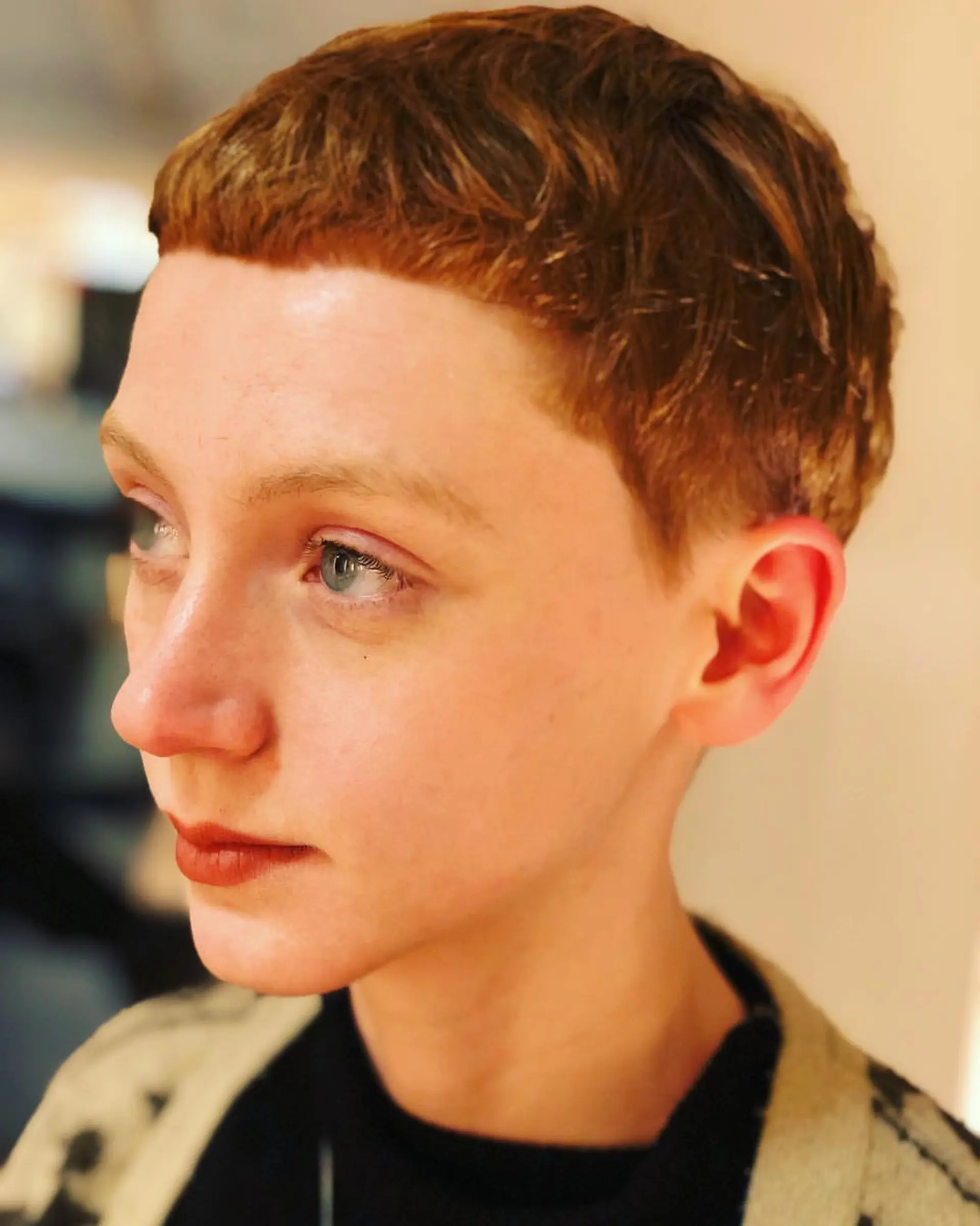 A very short auburn pixie cut with blunt micro bangs, tapered sides, and a defined hairline for a retro appearance. 1
