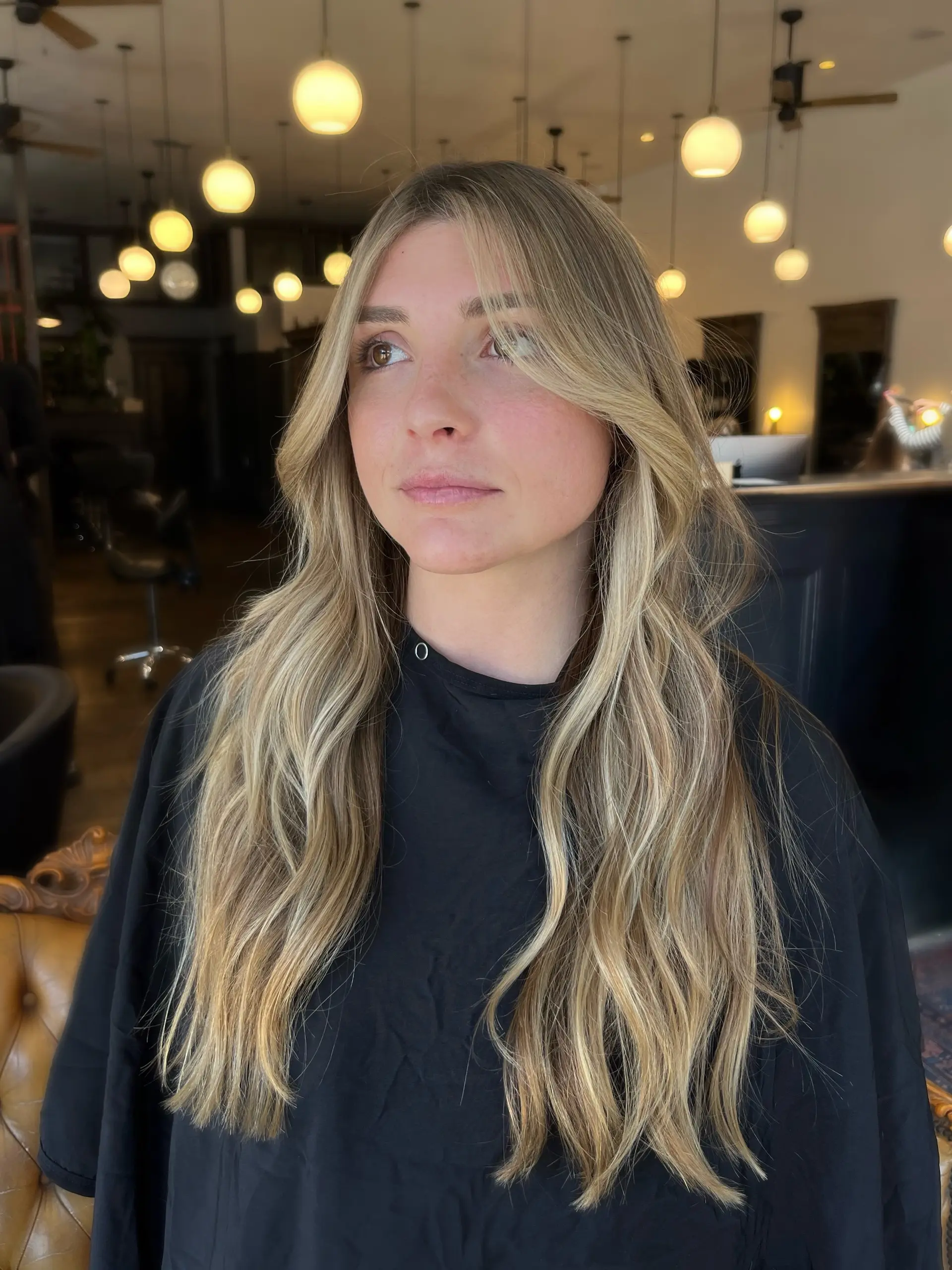 Long lived-in golden blonde hair styled in soft, natural waves with face-framing curtain bangs. 1